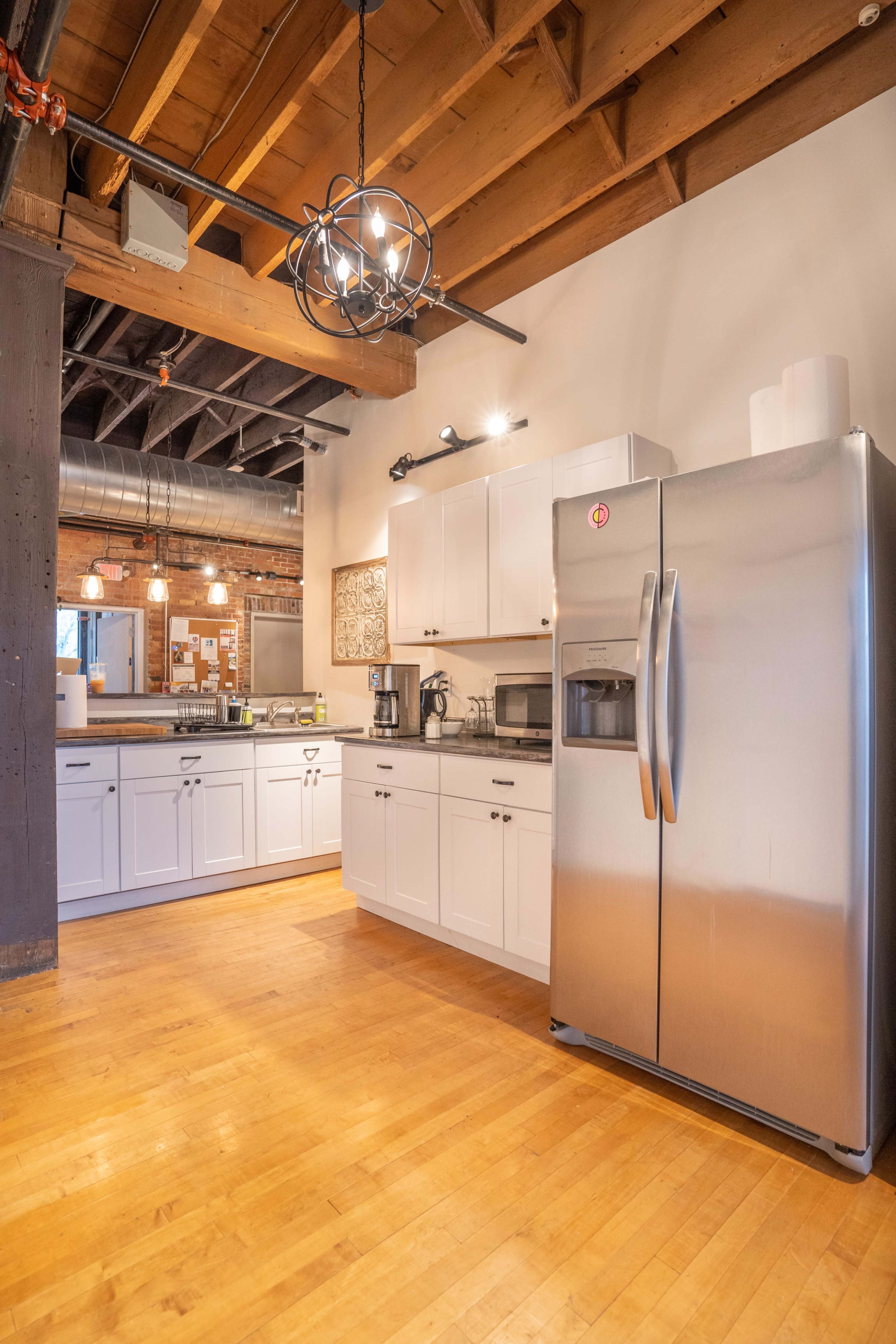The image shows a modern kitchen with white cabinetry, stainless steel appliances, and exposed wooden beams.