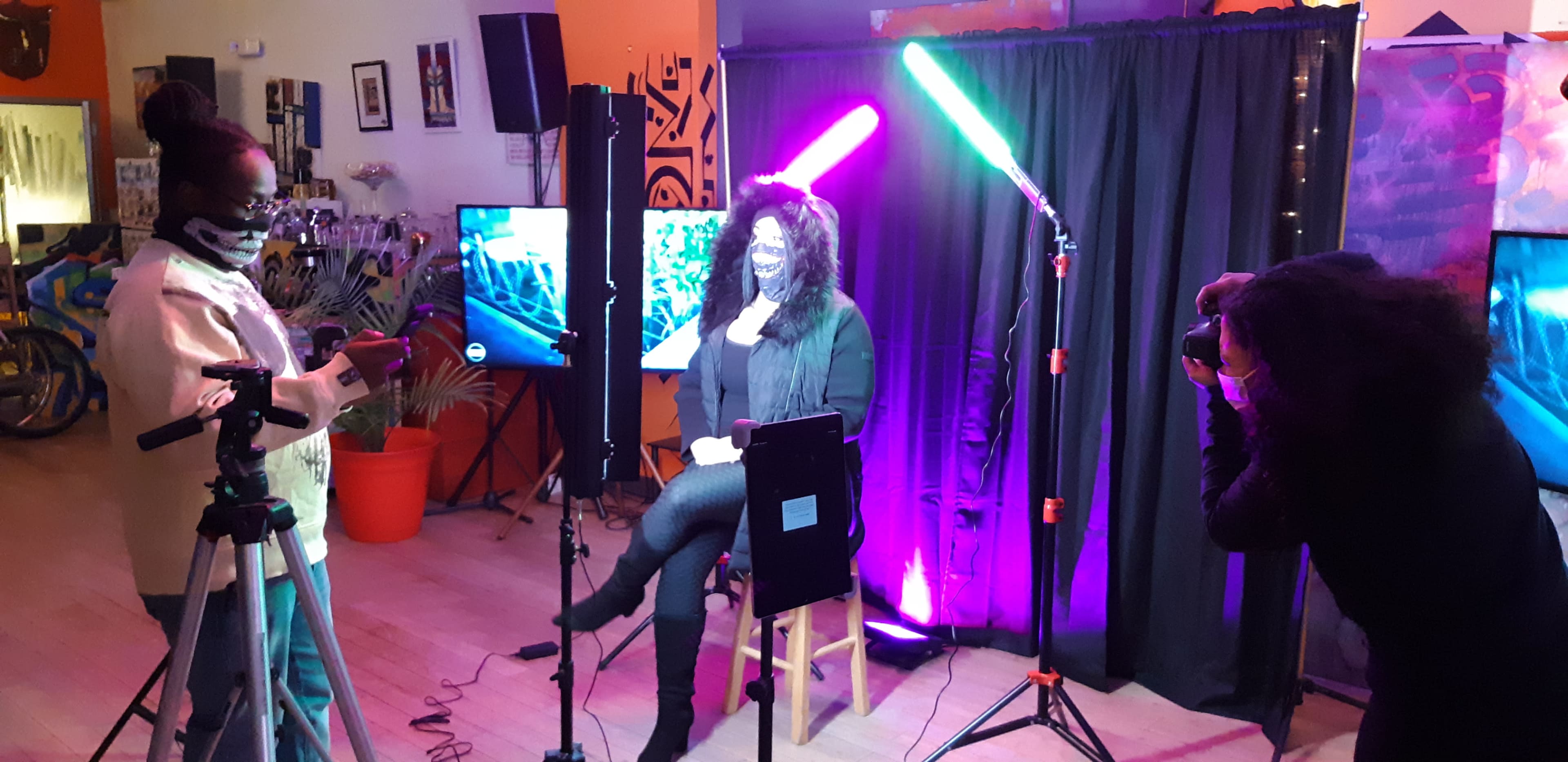 A photographer captures a portrait of a woman seated against a backdrop with colorful lighting, while another person sets up equipment nearby.