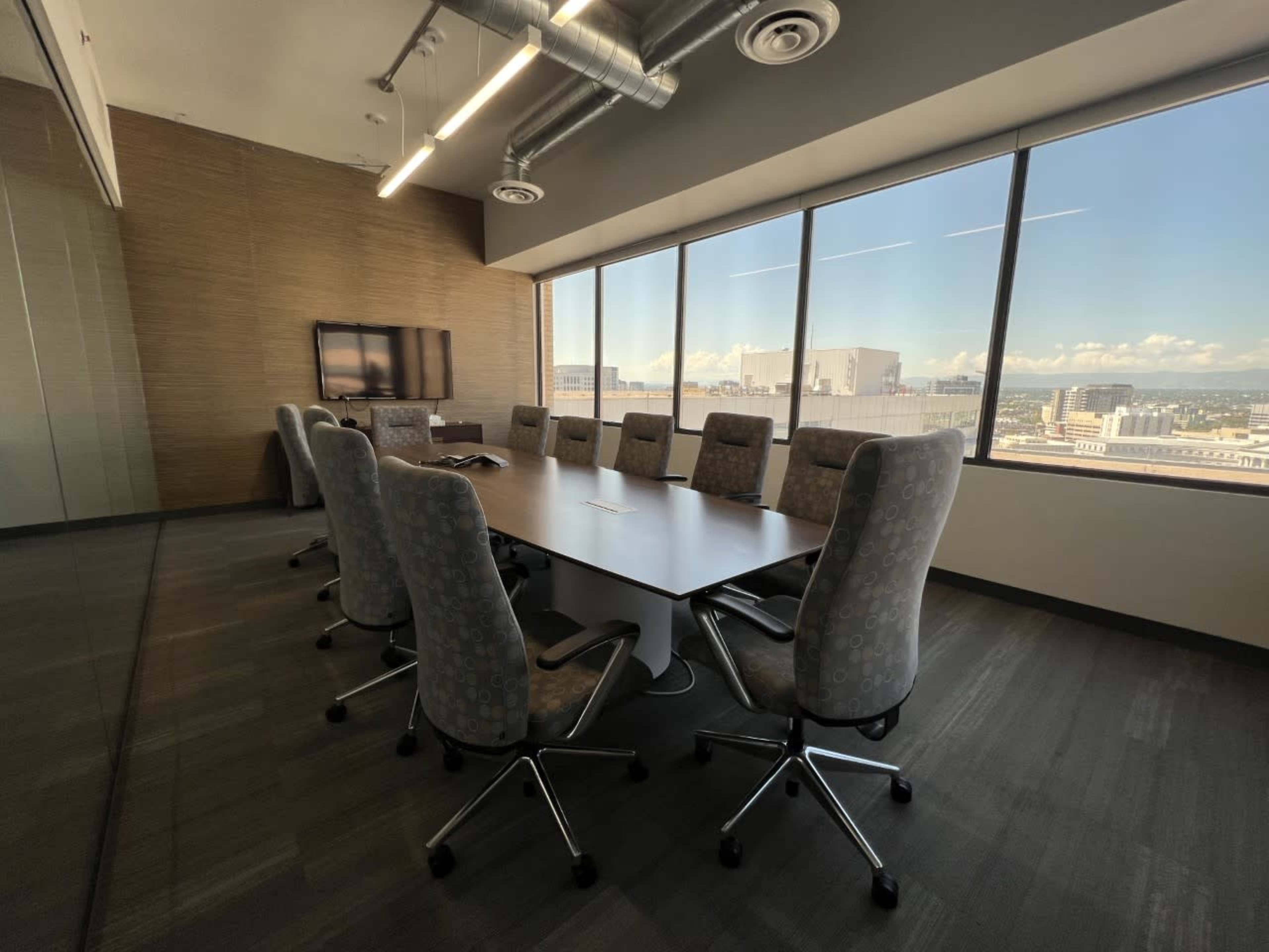 A modern conference room features a large table surrounded by ten ergonomic chairs, with floor-to-ceiling windows showcasing a city view.