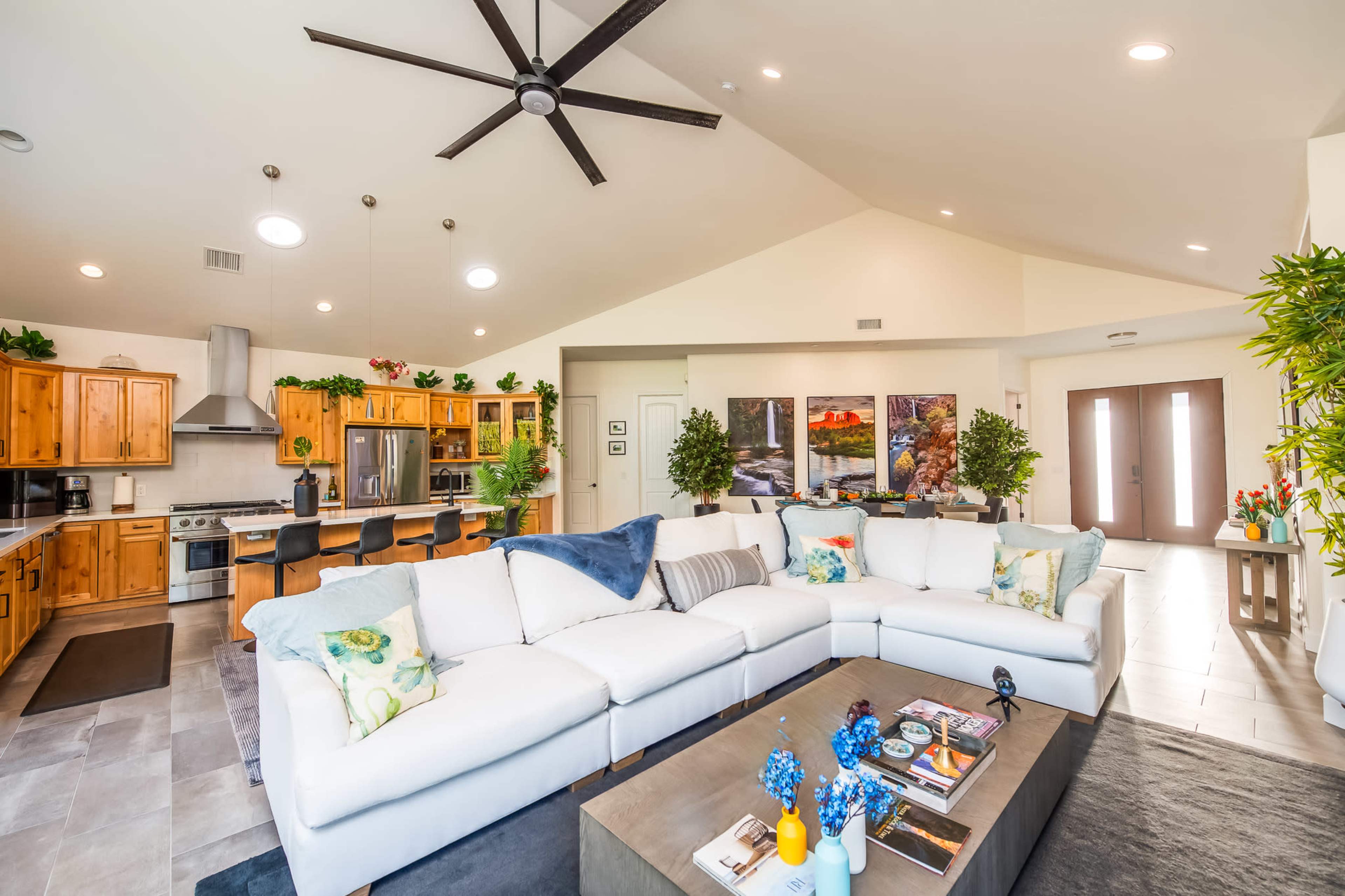 A spacious living area featuring a large sectional sofa, a coffee table with magazines, and a kitchen with wooden cabinetry and a ventilation hood.