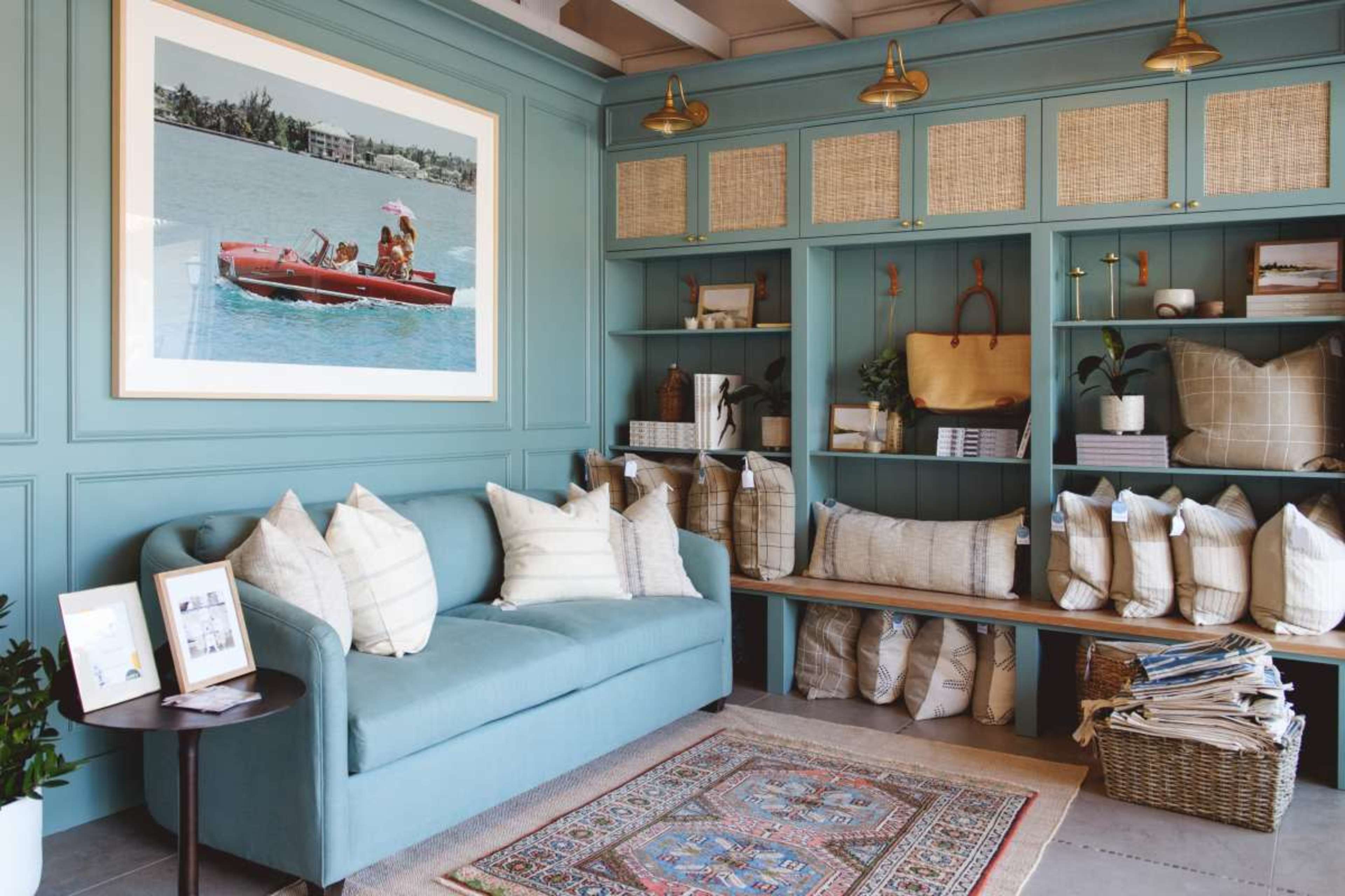 A light blue sofa is positioned against a wall decorated with shelves filled with pillows and decorative items, alongside a large framed photo of a boat on water.