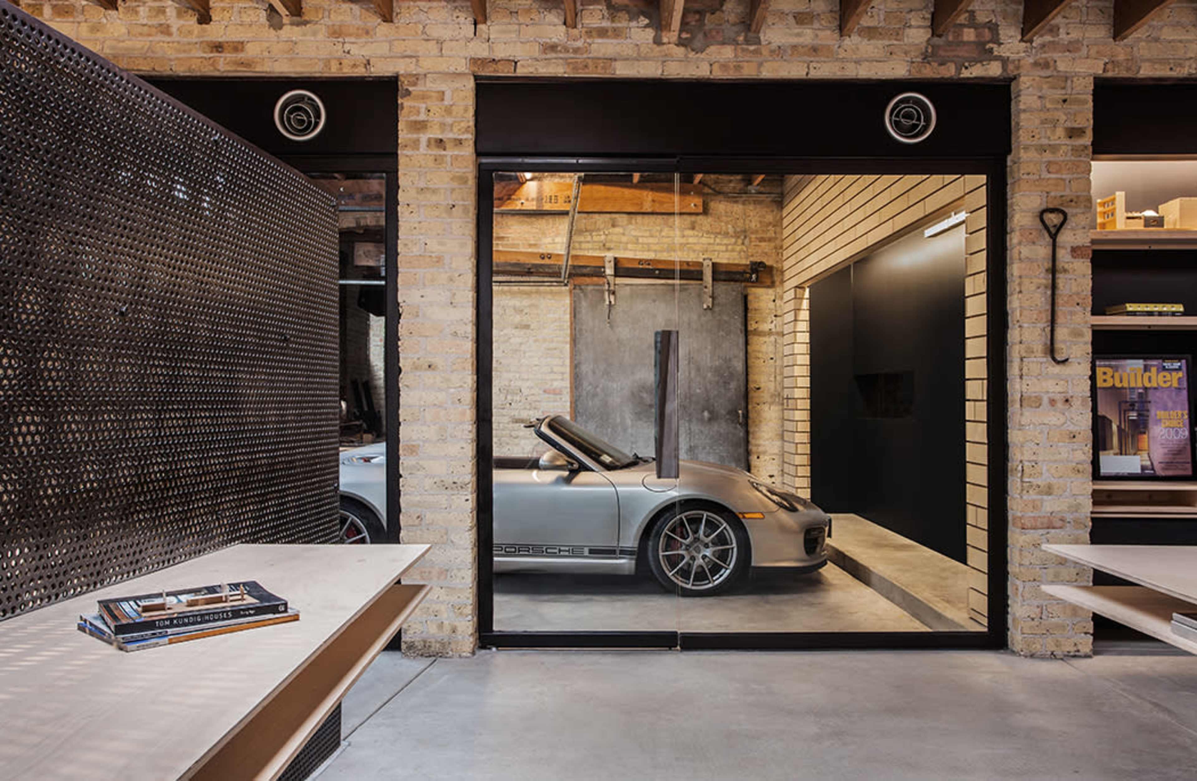 A sleek silver sports car is parked in a modern garage with exposed brick walls and large glass doors.