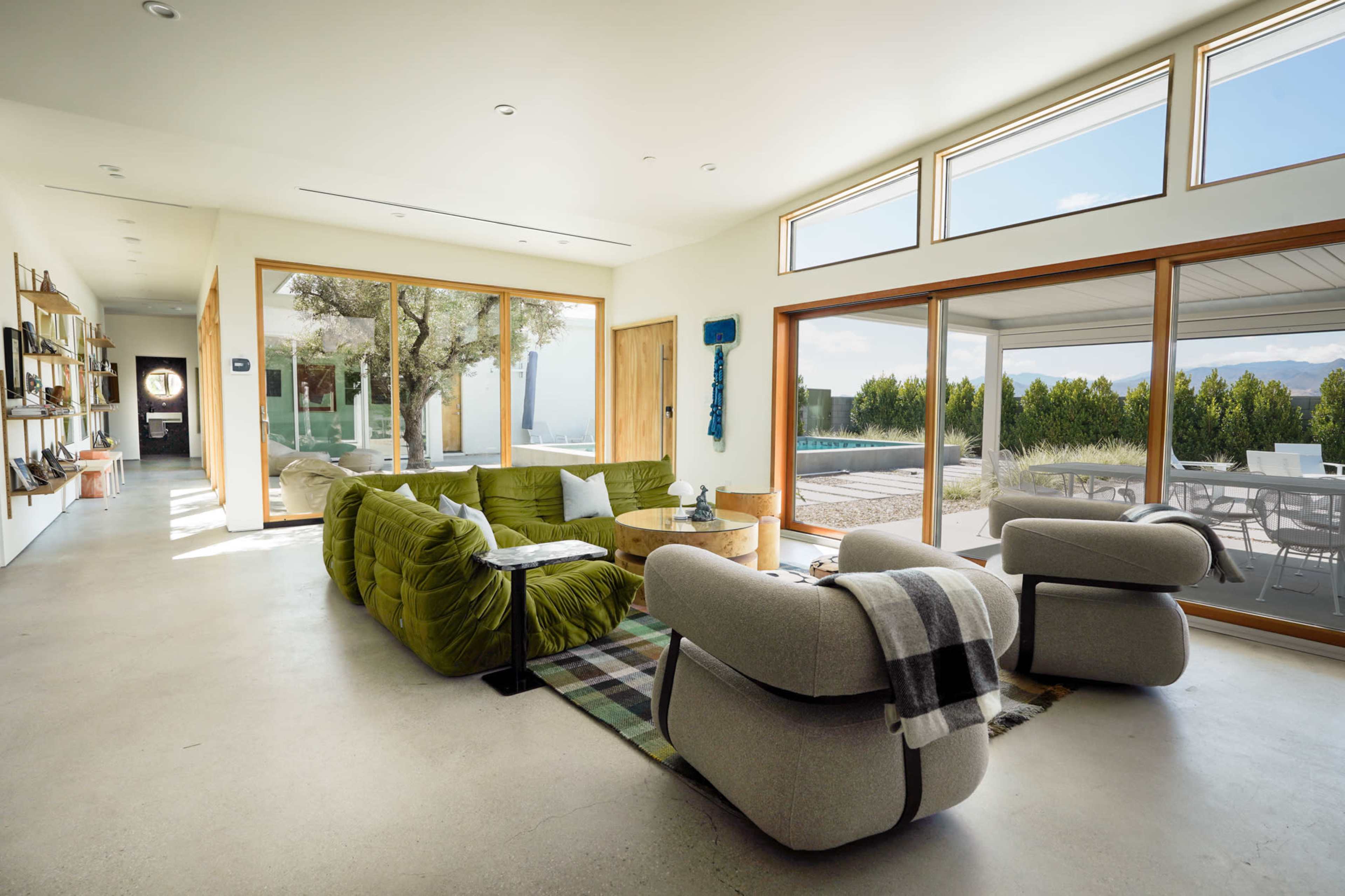 The spacious living room features large windows, a green sectional sofa, and natural light filling the modern space.