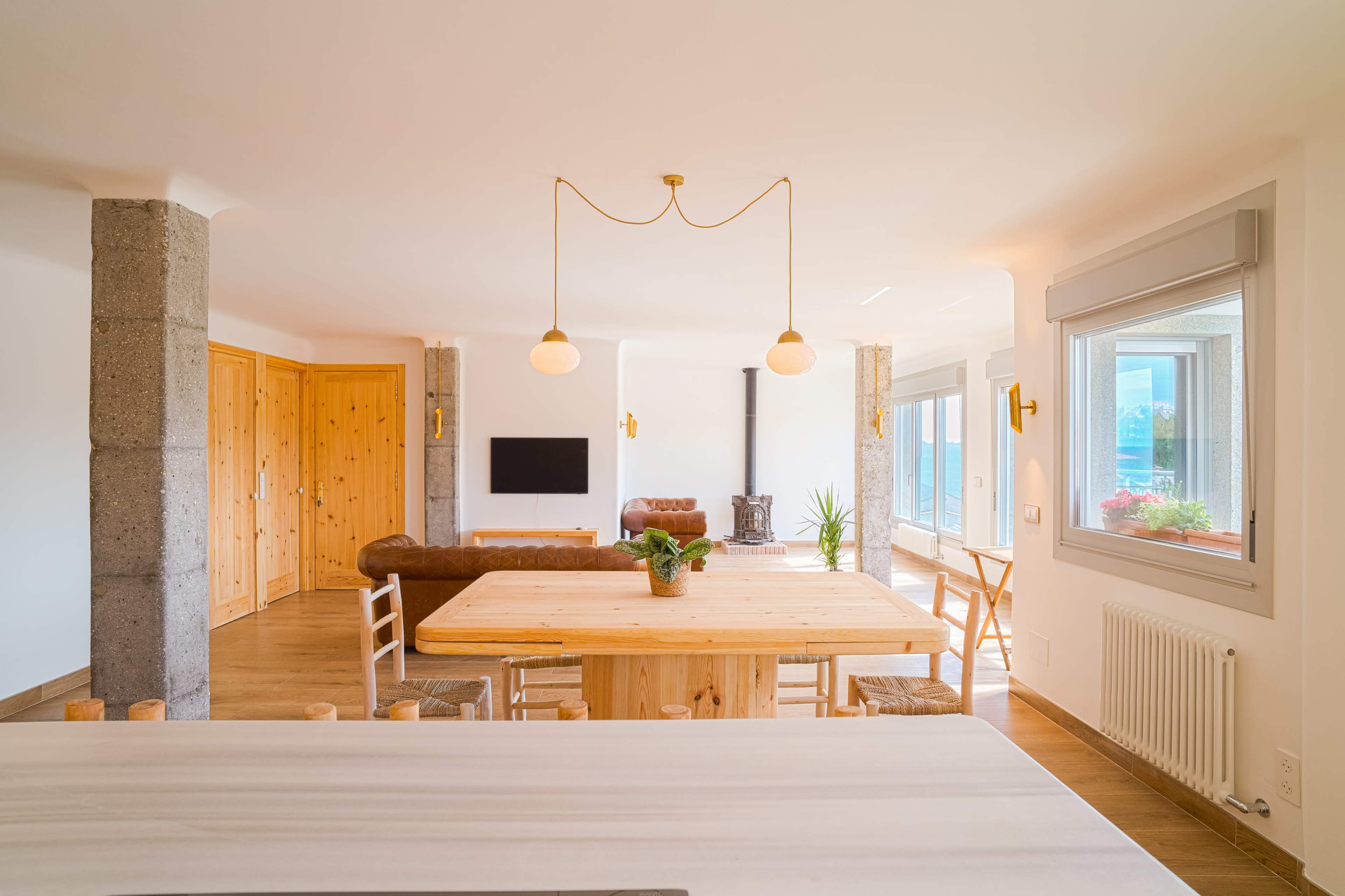 The image shows a modern dining area featuring a wooden table, light-colored walls, and a cozy wood stove in the background.