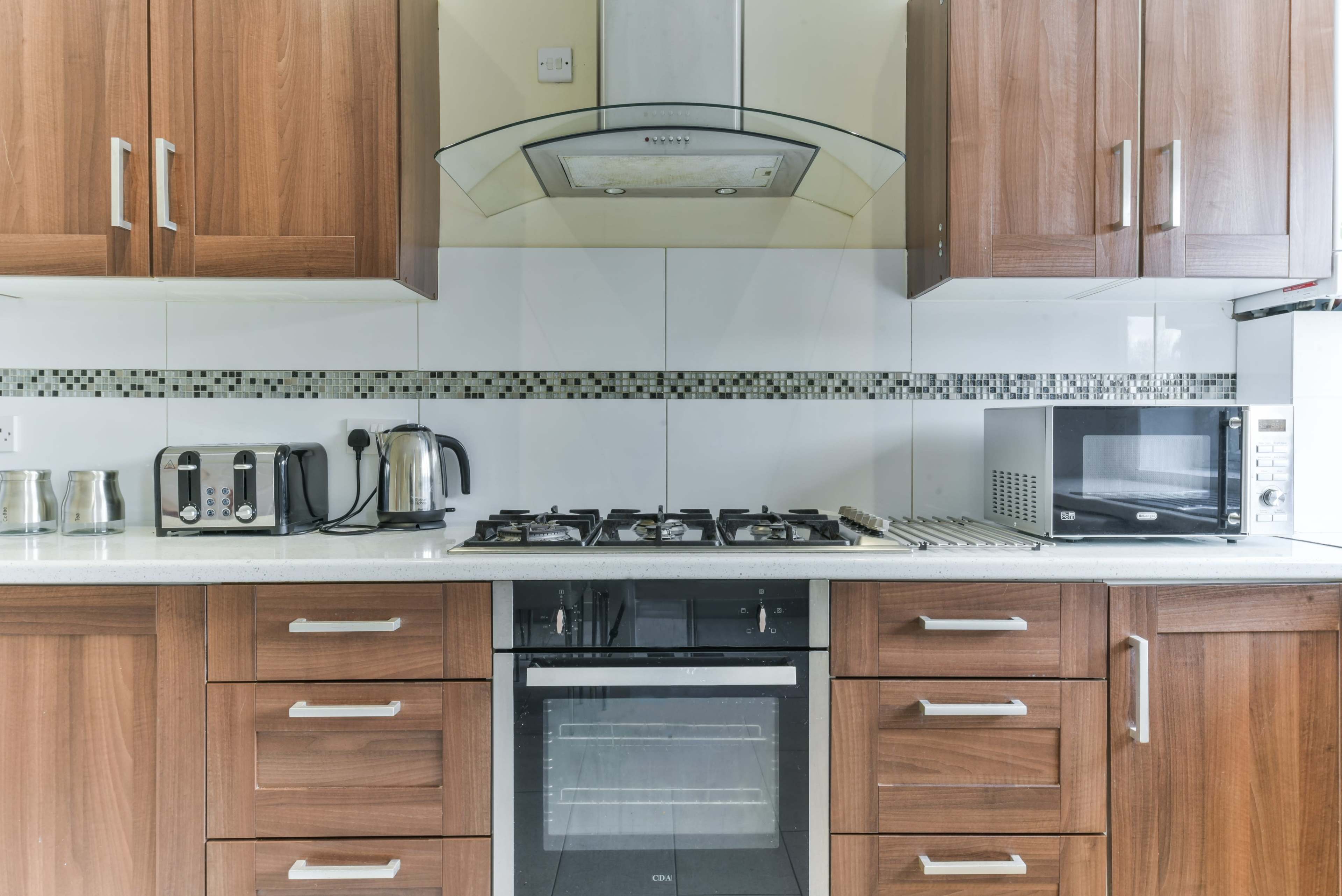 A modern kitchen with wooden cabinets, a gas stove, a microwave, a toaster, and a kettle arranged on a countertop.