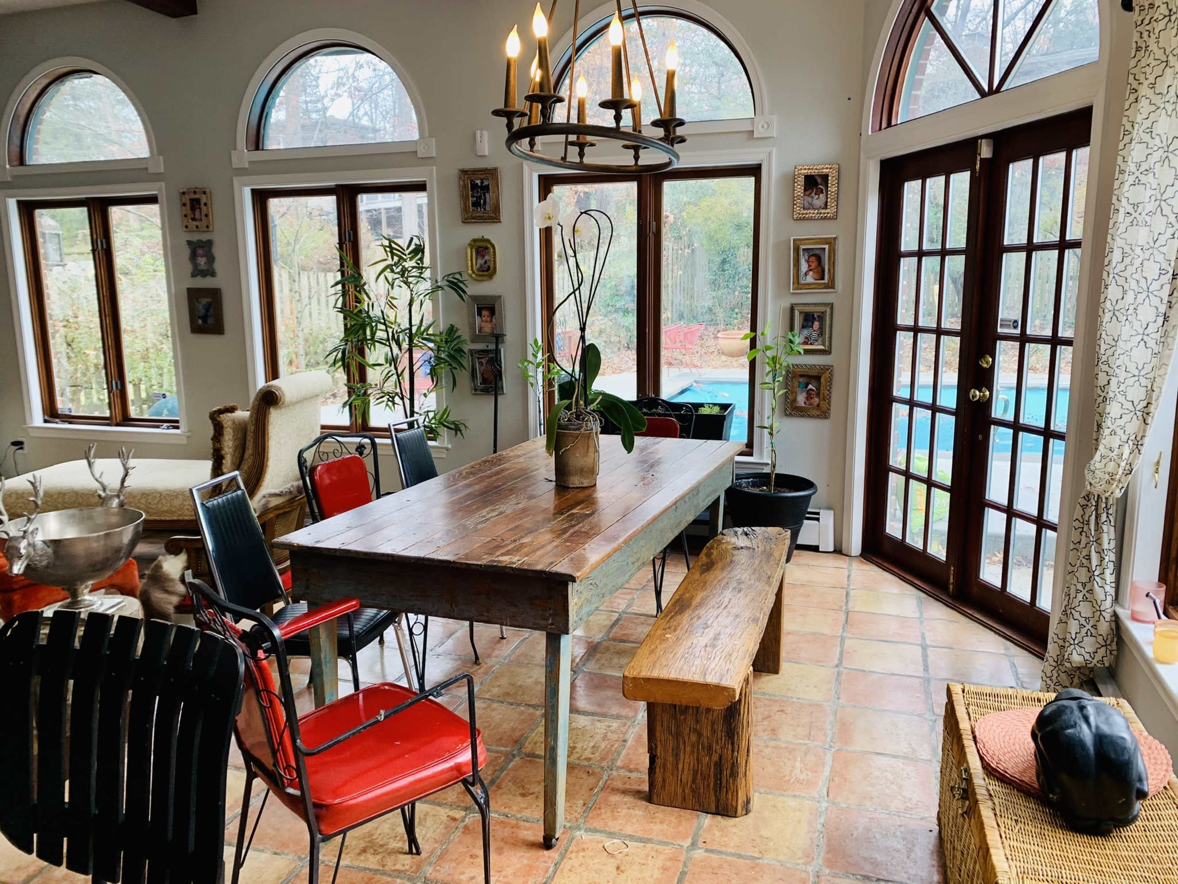 A dining area with a wooden table surrounded by various chairs, a bench, and large windows that overlook a garden.