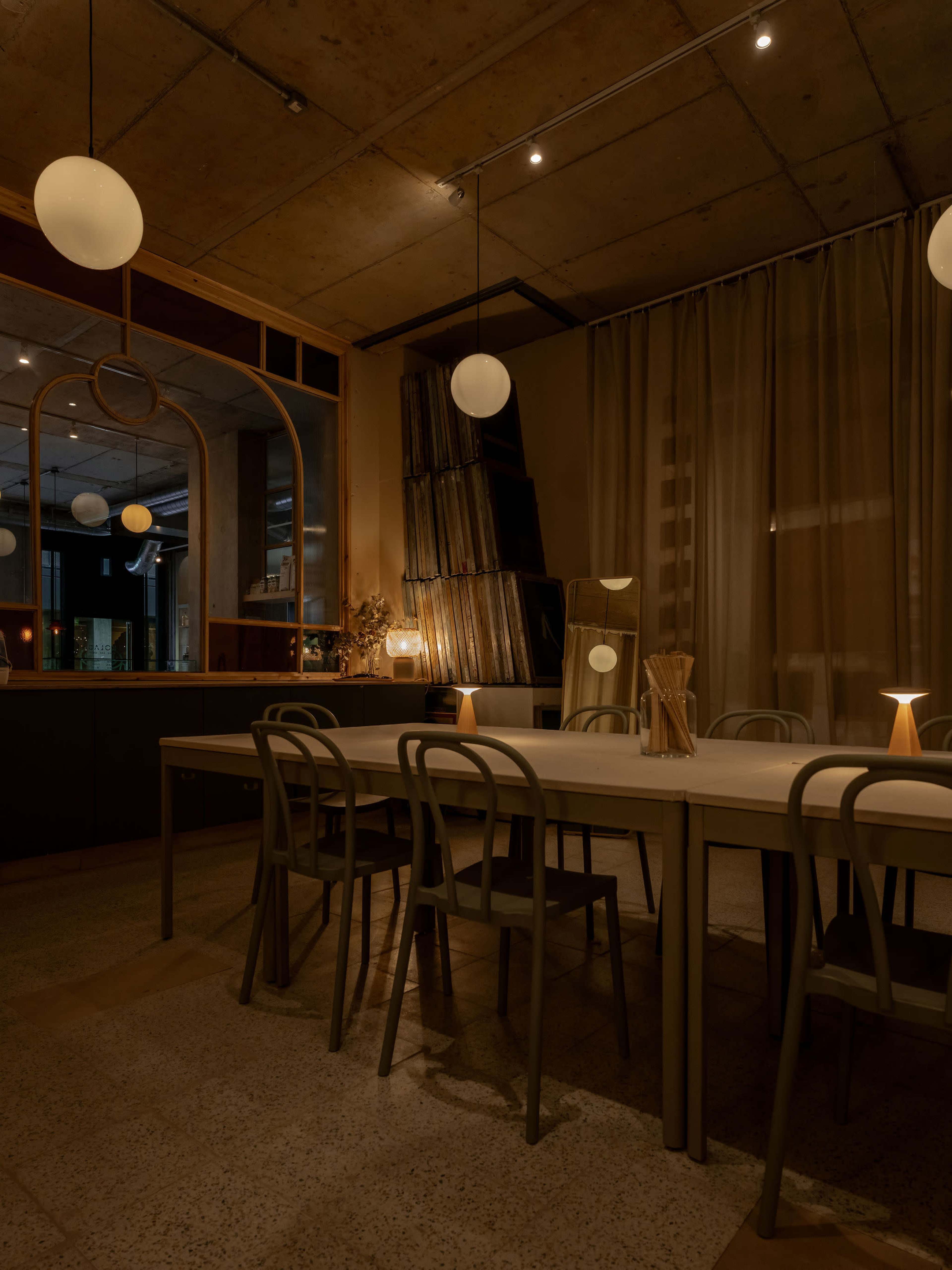 The image shows a dimly lit dining area with a long table surrounded by chairs, featuring a large mirror and decorative elements on the walls.