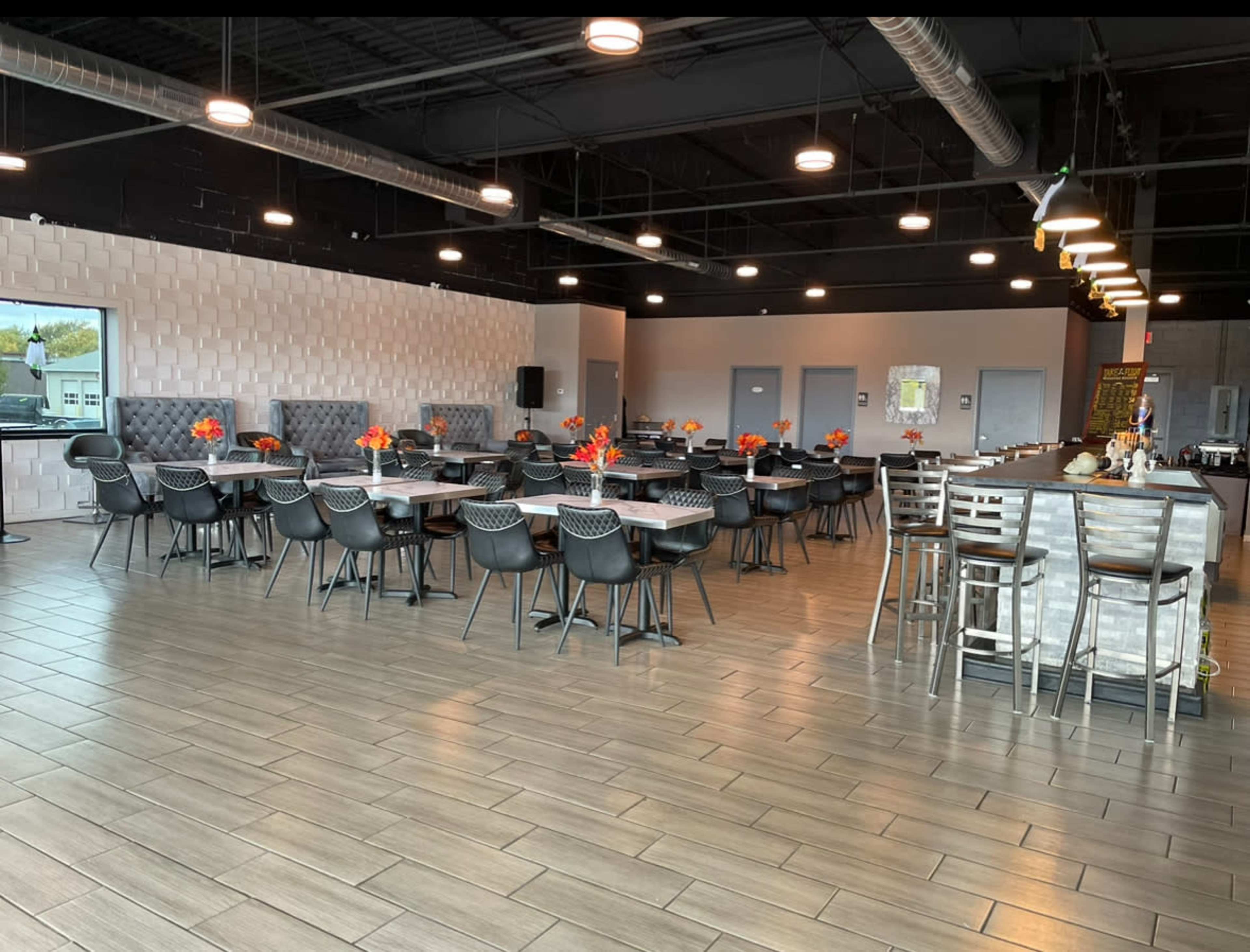 The image shows a spacious restaurant interior with several tables set for dining, featuring gray booths along the walls and a bar area in the background.