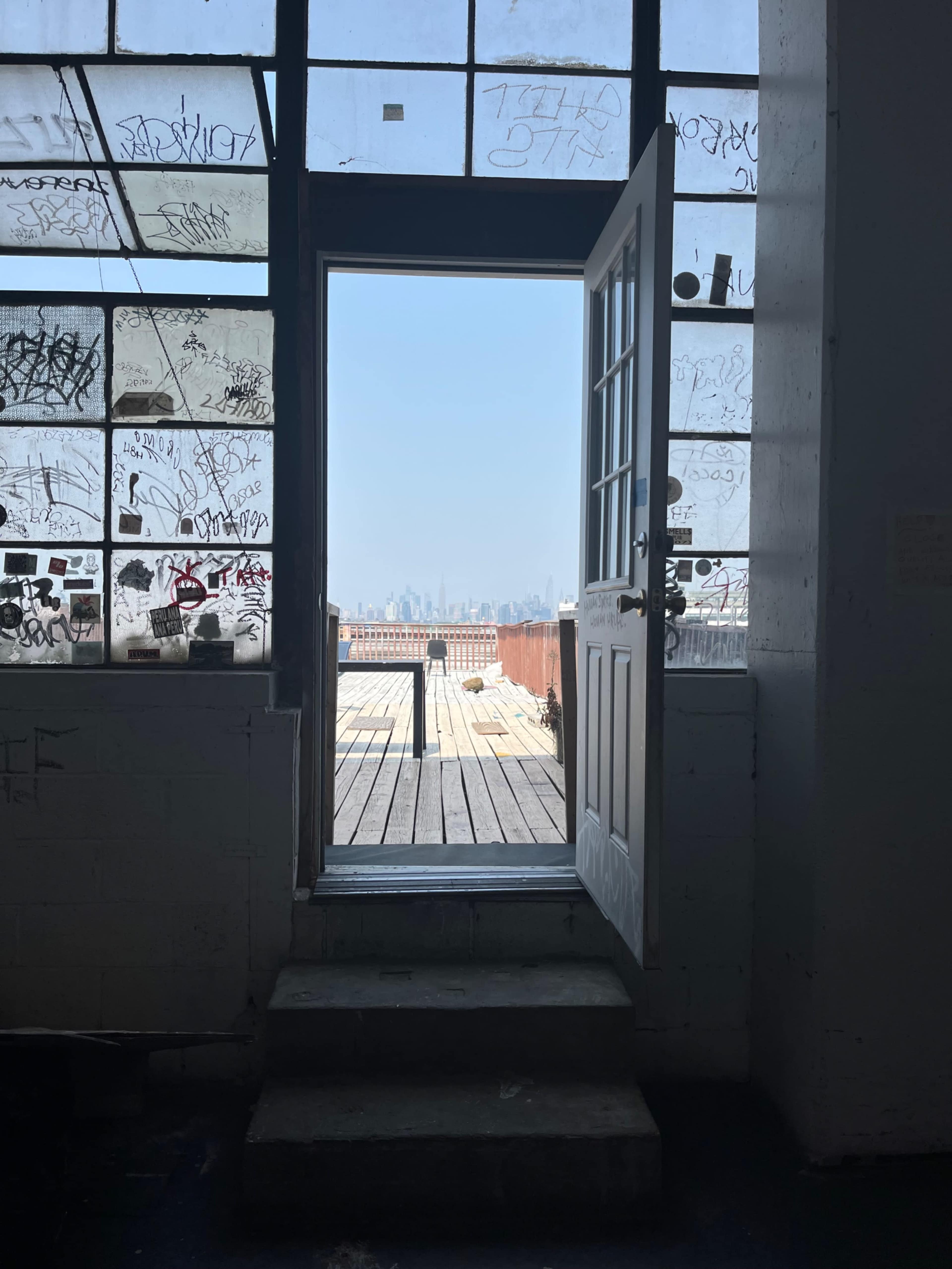 A door opens to a view of a city skyline through large, partially graffiti-covered windows.