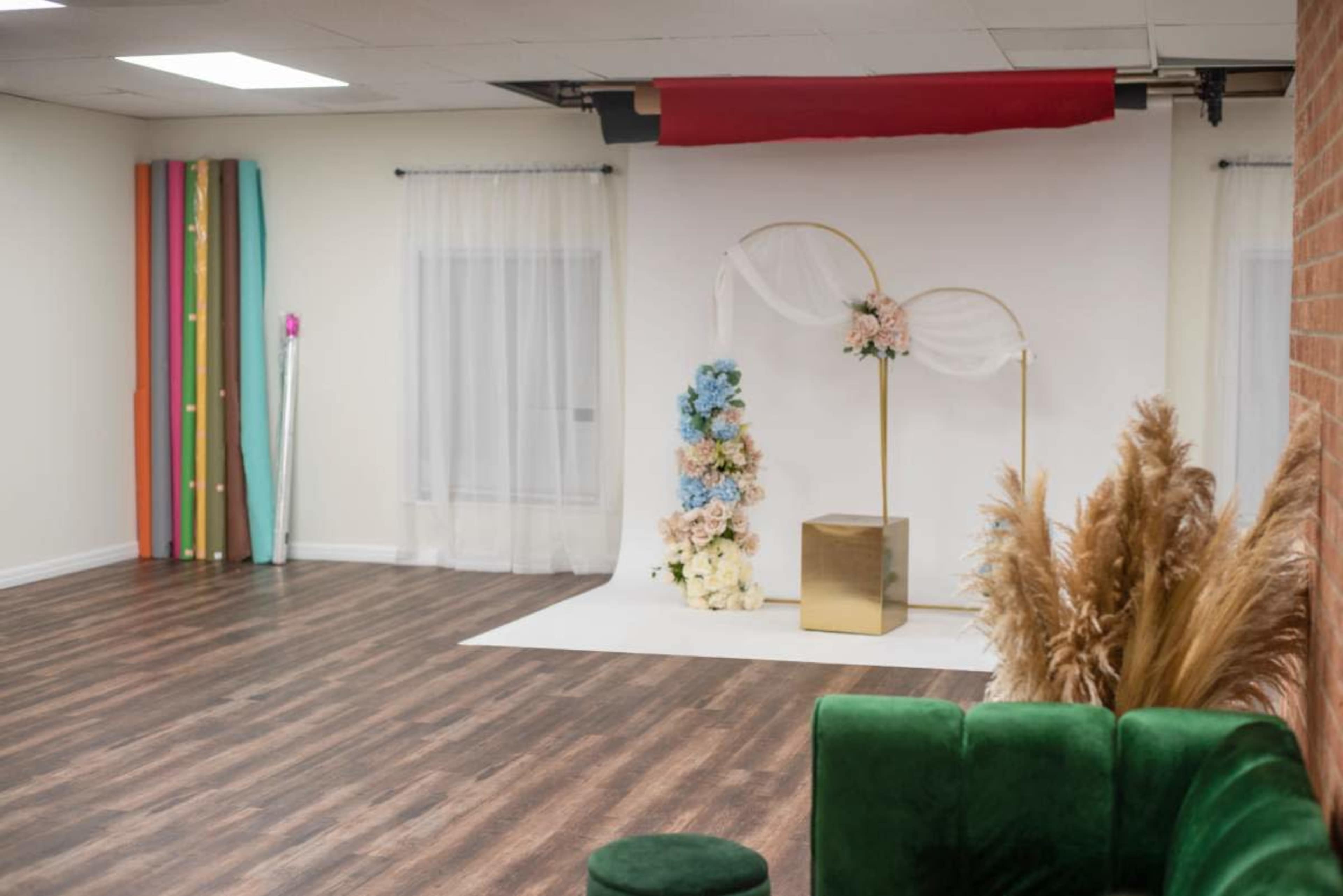The image shows a spacious, well-lit room featuring a floral display on a backdrop, decorative plants, and colorful vertical stripes along the walls.
