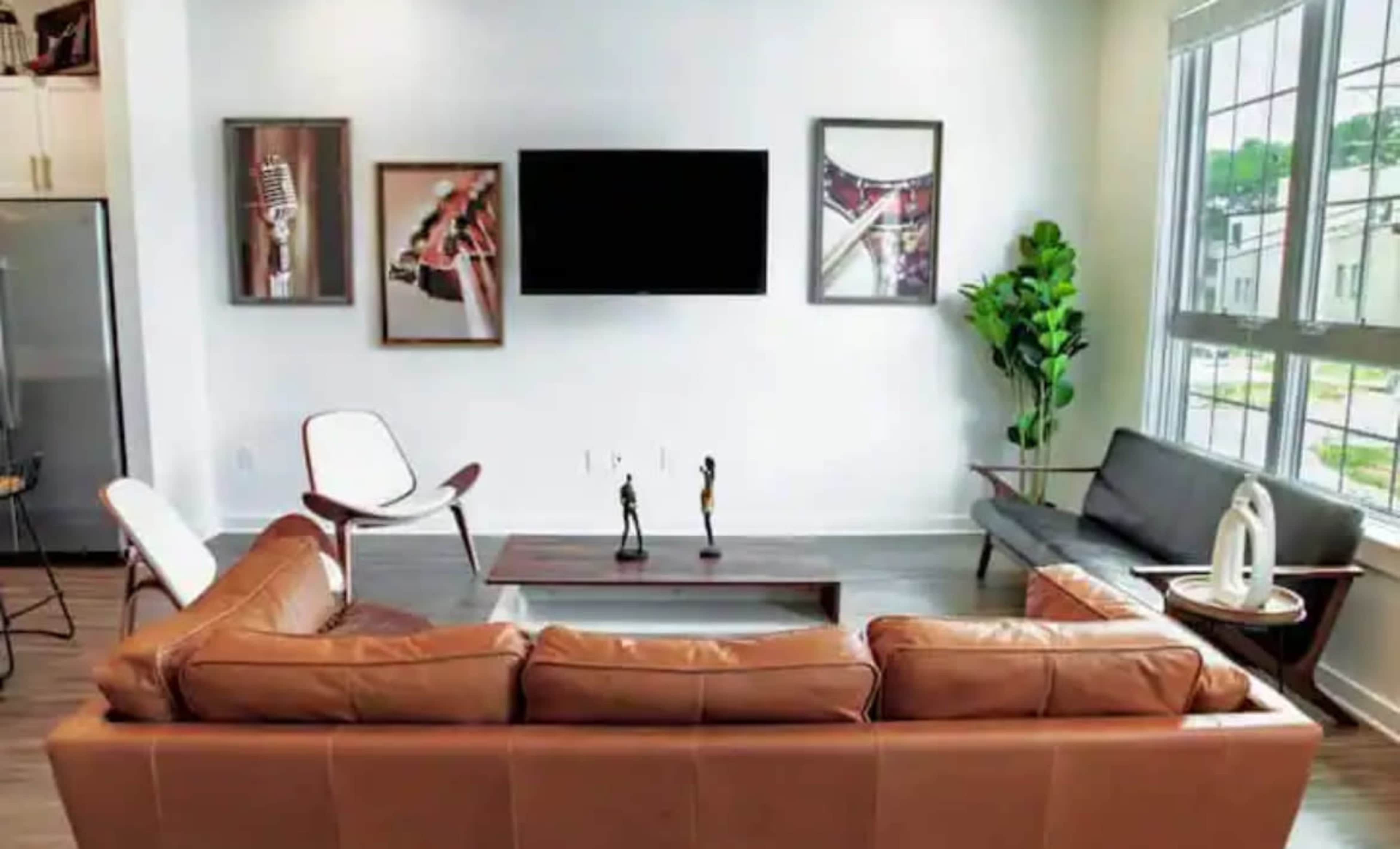A modern living room featuring a brown leather sofa, a coffee table, framed artwork on the walls, and a large television mounted above.