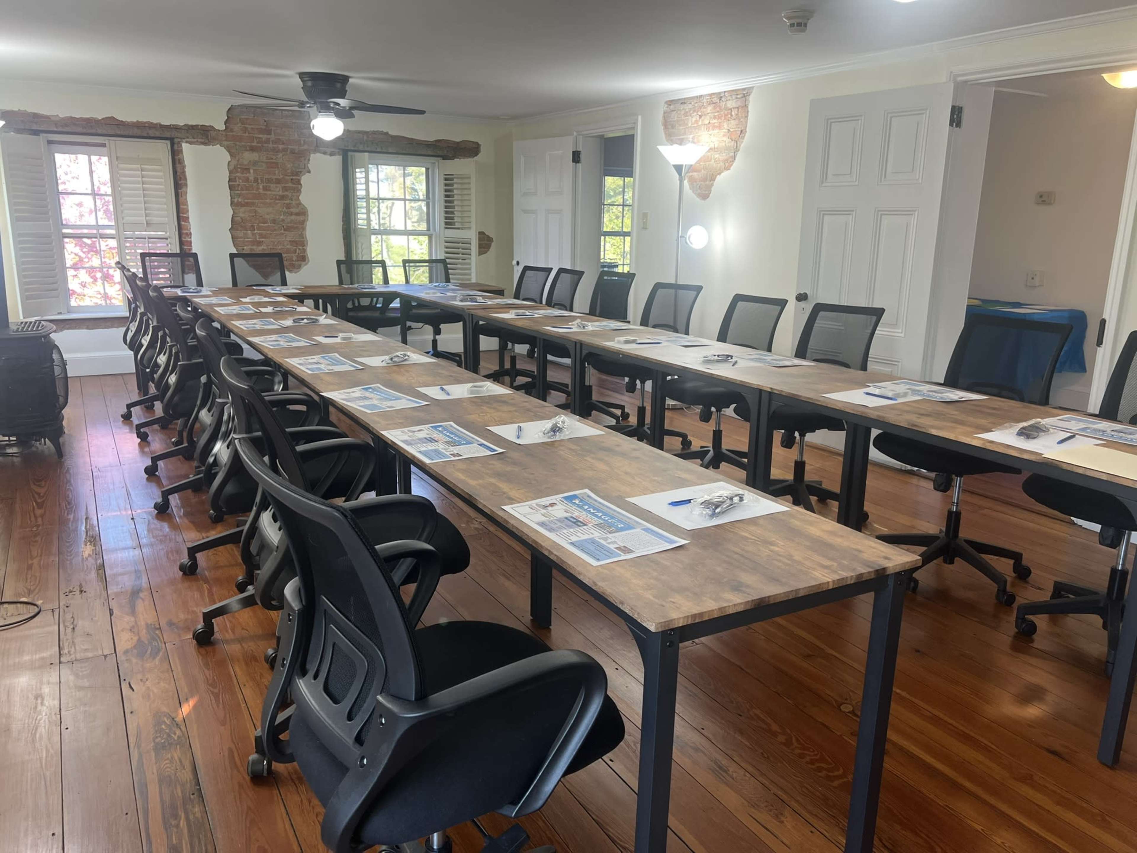 The image shows a spacious conference room set up with multiple tables arranged in rows, each equipped with chairs and materials for a meeting.