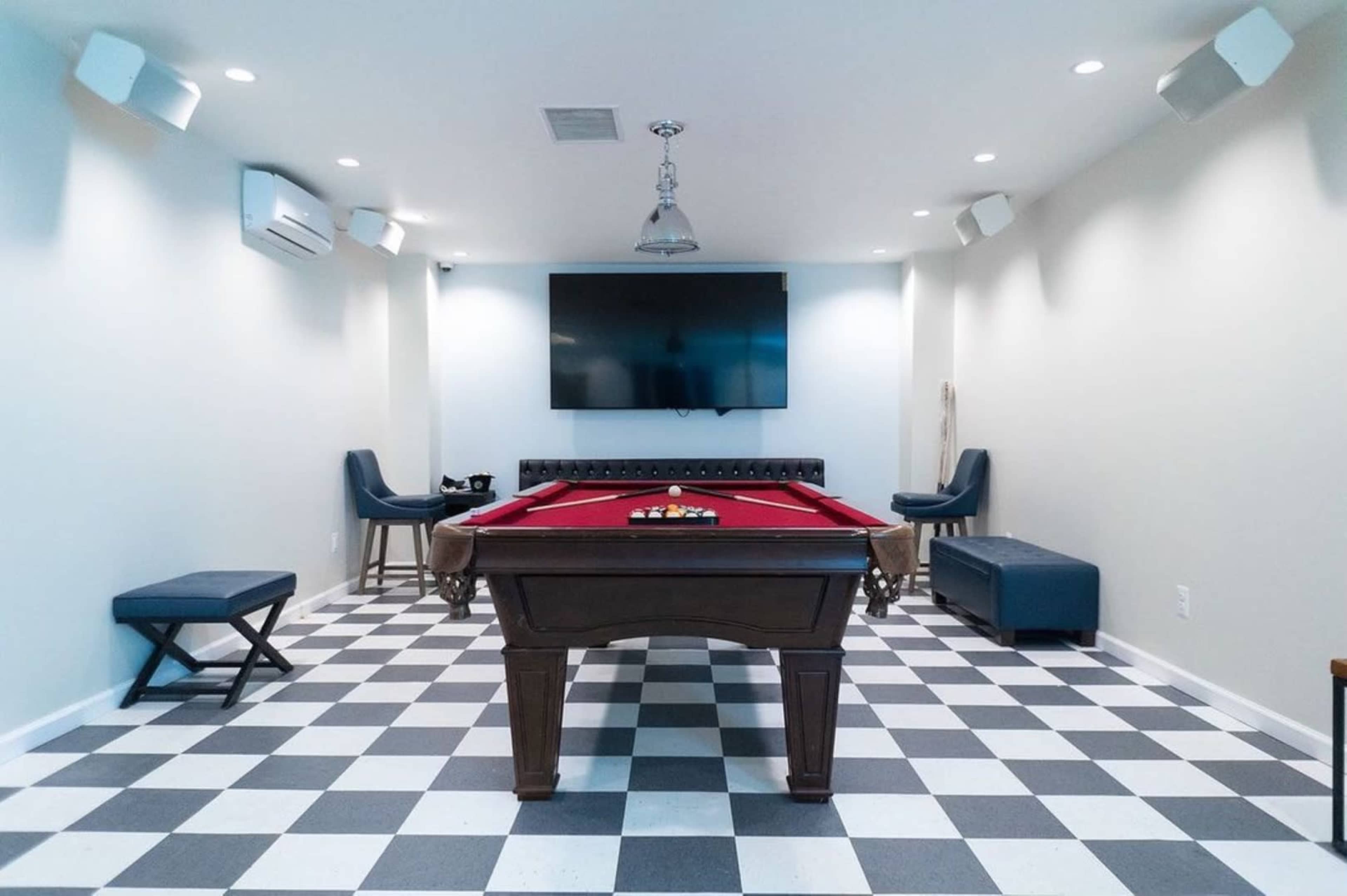 A recreational room featuring a billiard table, a large wall-mounted television, and seating arranged around the space.