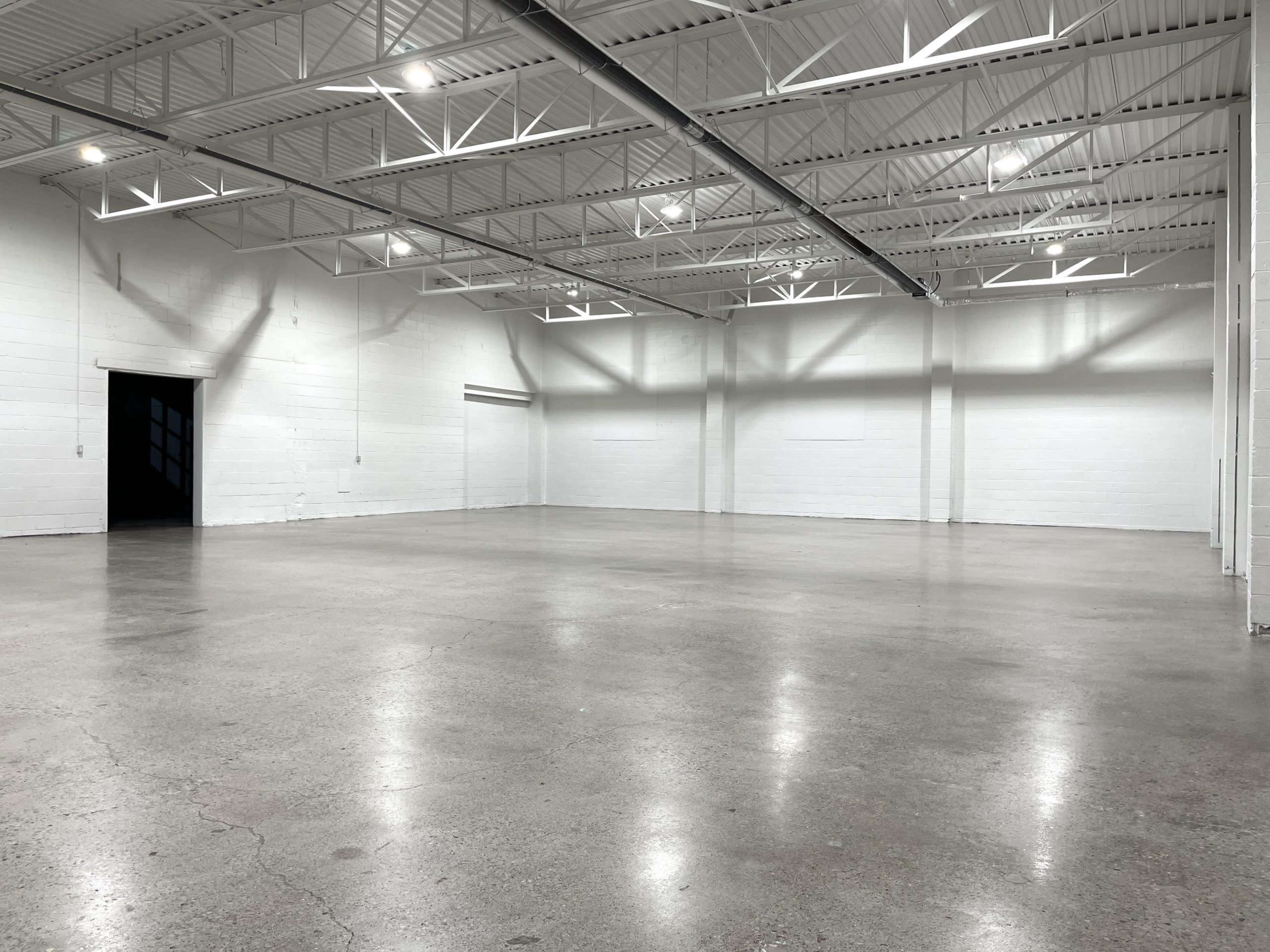 The image shows an empty warehouse space with a polished concrete floor and white walls.