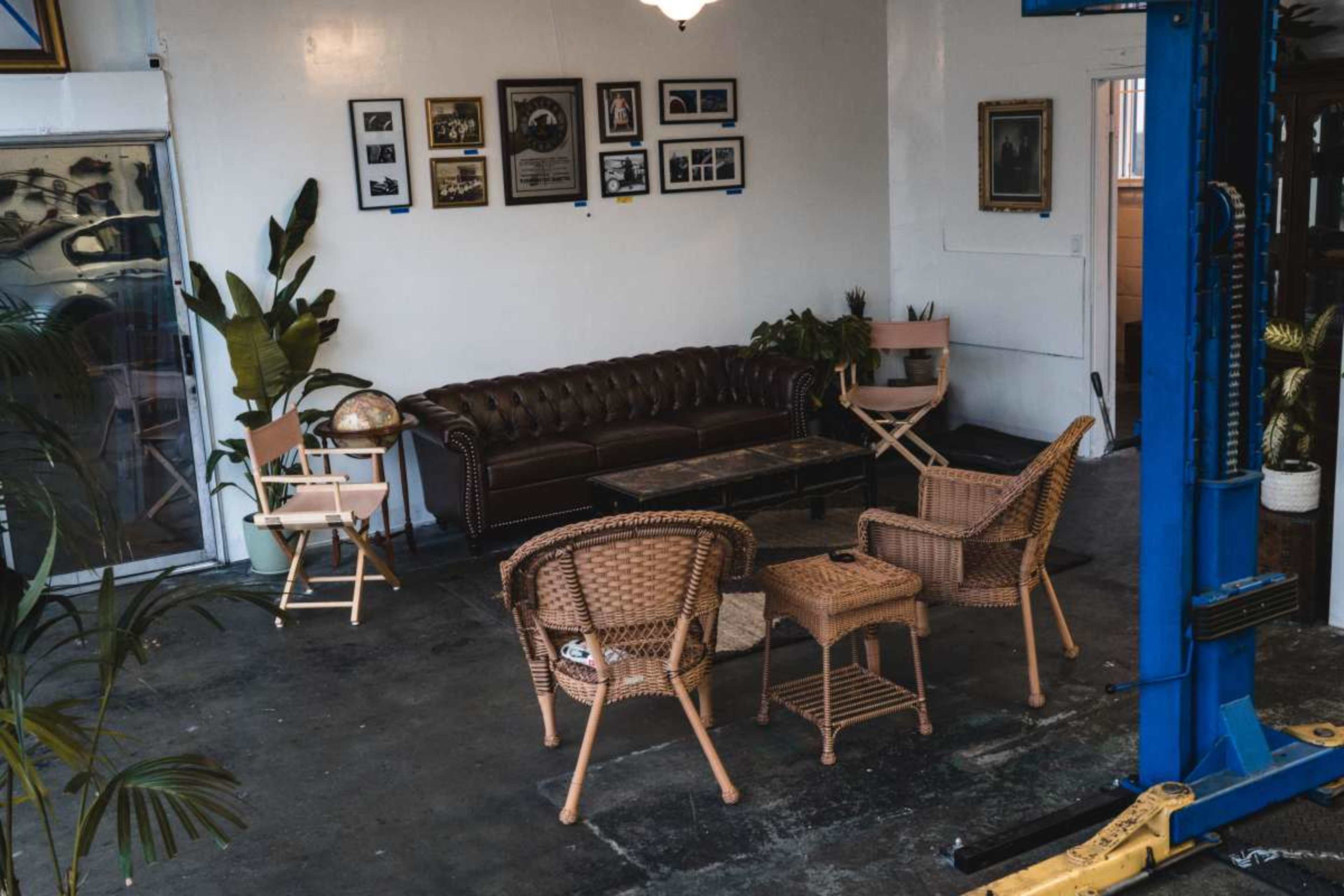 The image shows a waiting area featuring a brown leather sofa, a coffee table, and various chairs, complemented by framed photographs on the wall and potted plants.