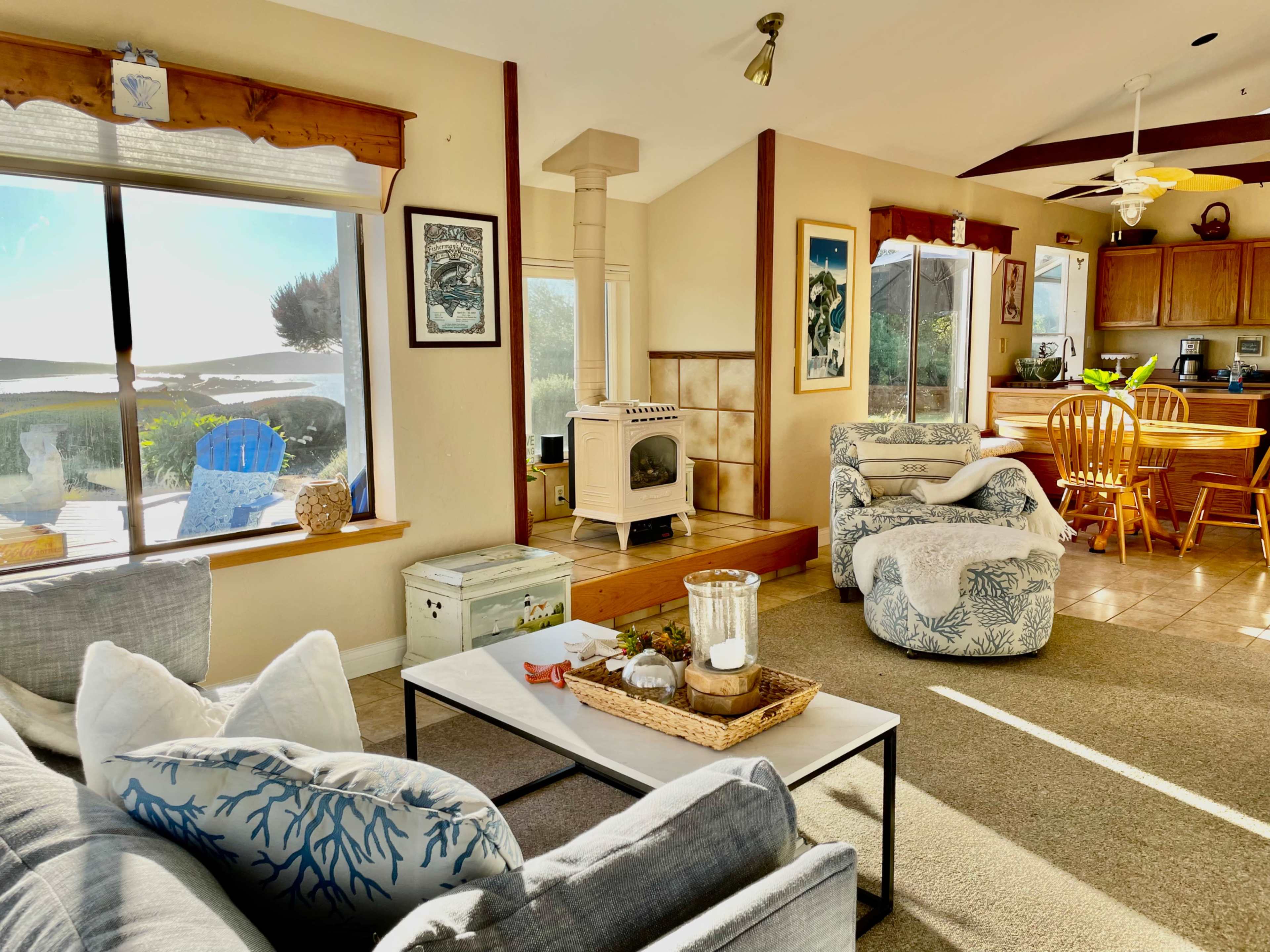 A cozy living area with a view of the outdoors, featuring a couch, a coffee table, and a wooden dining area in the background.