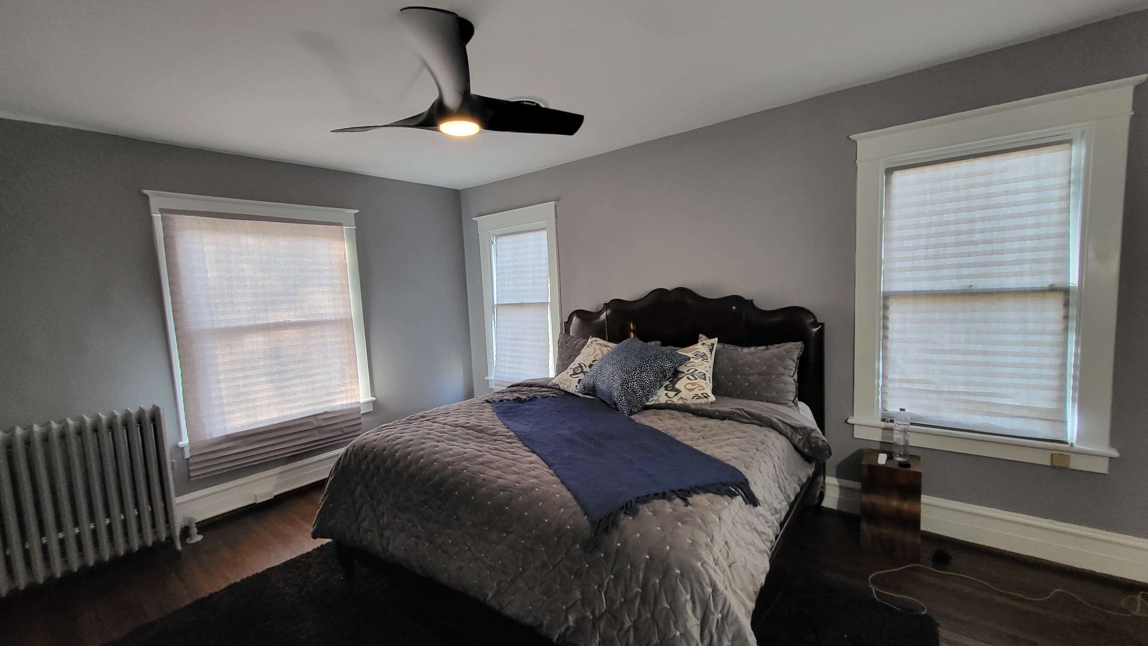 A bedroom featuring a bed with a dark gray quilt, a blue throw blanket, and two windows with white blinds.