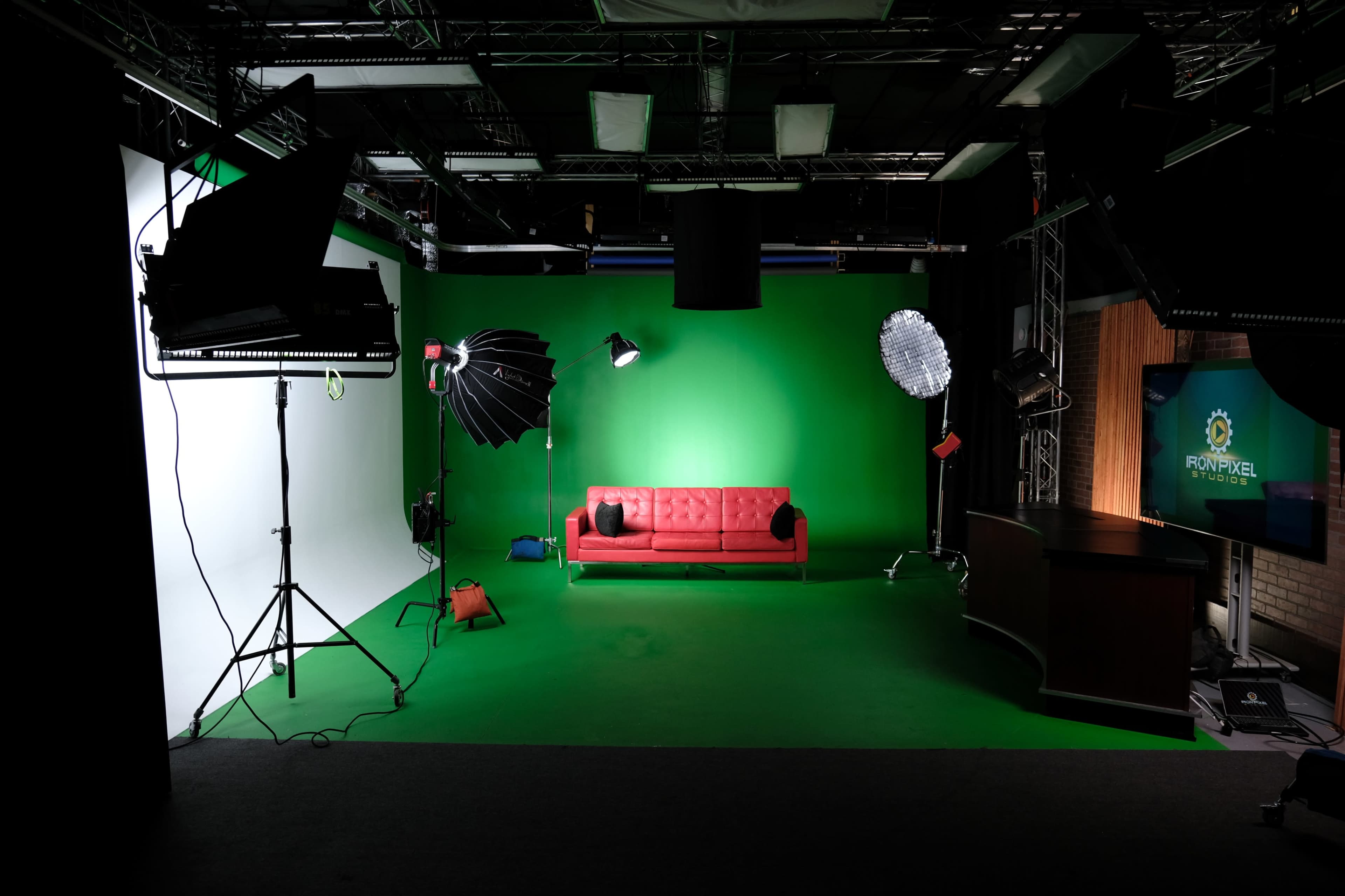 A television studio with a green backdrop, a red couch in the center, and various lighting equipment arranged around the space.