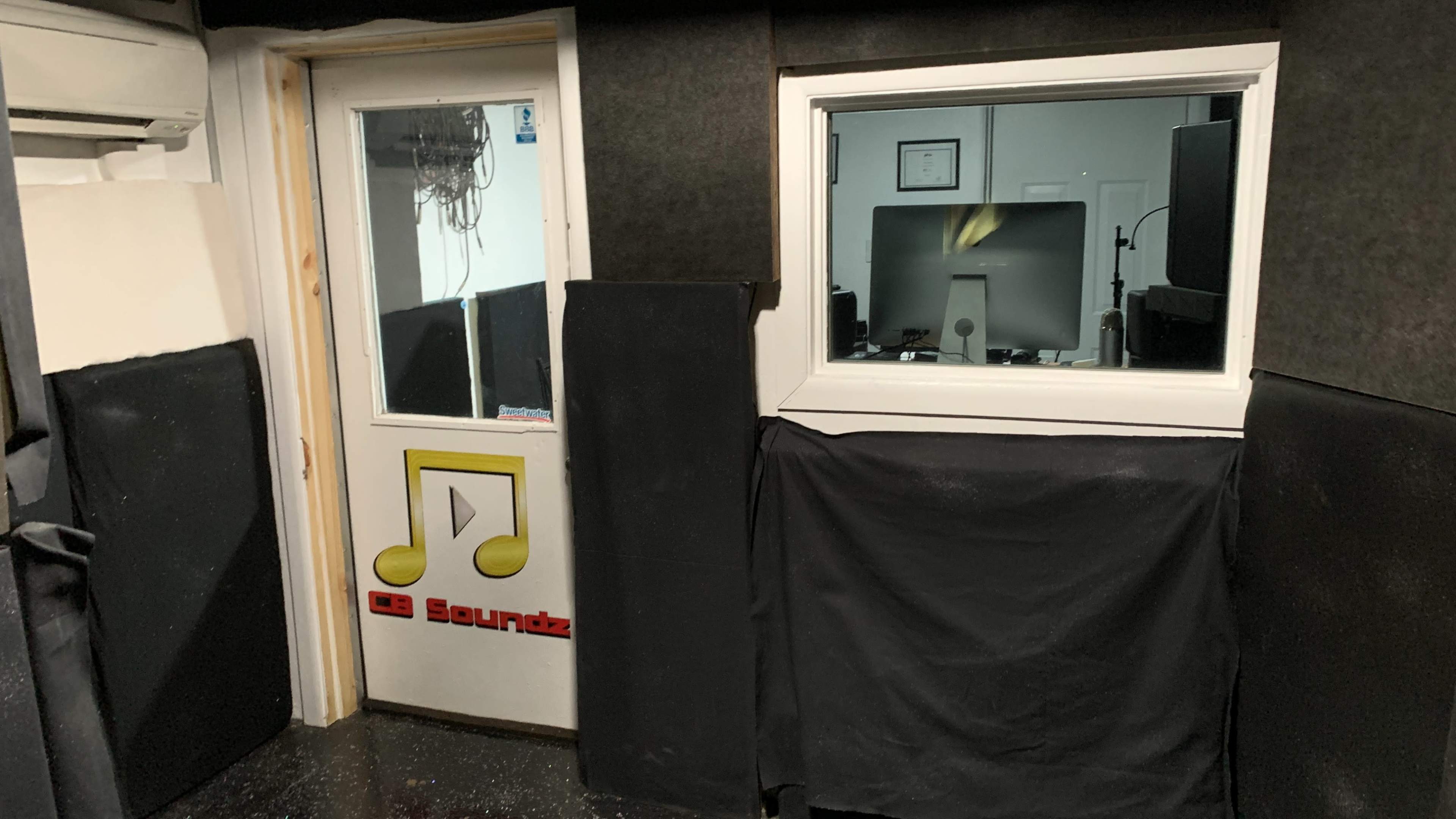 The image shows a soundproof recording studio entrance with a glass window and a door marked with a music note logo.