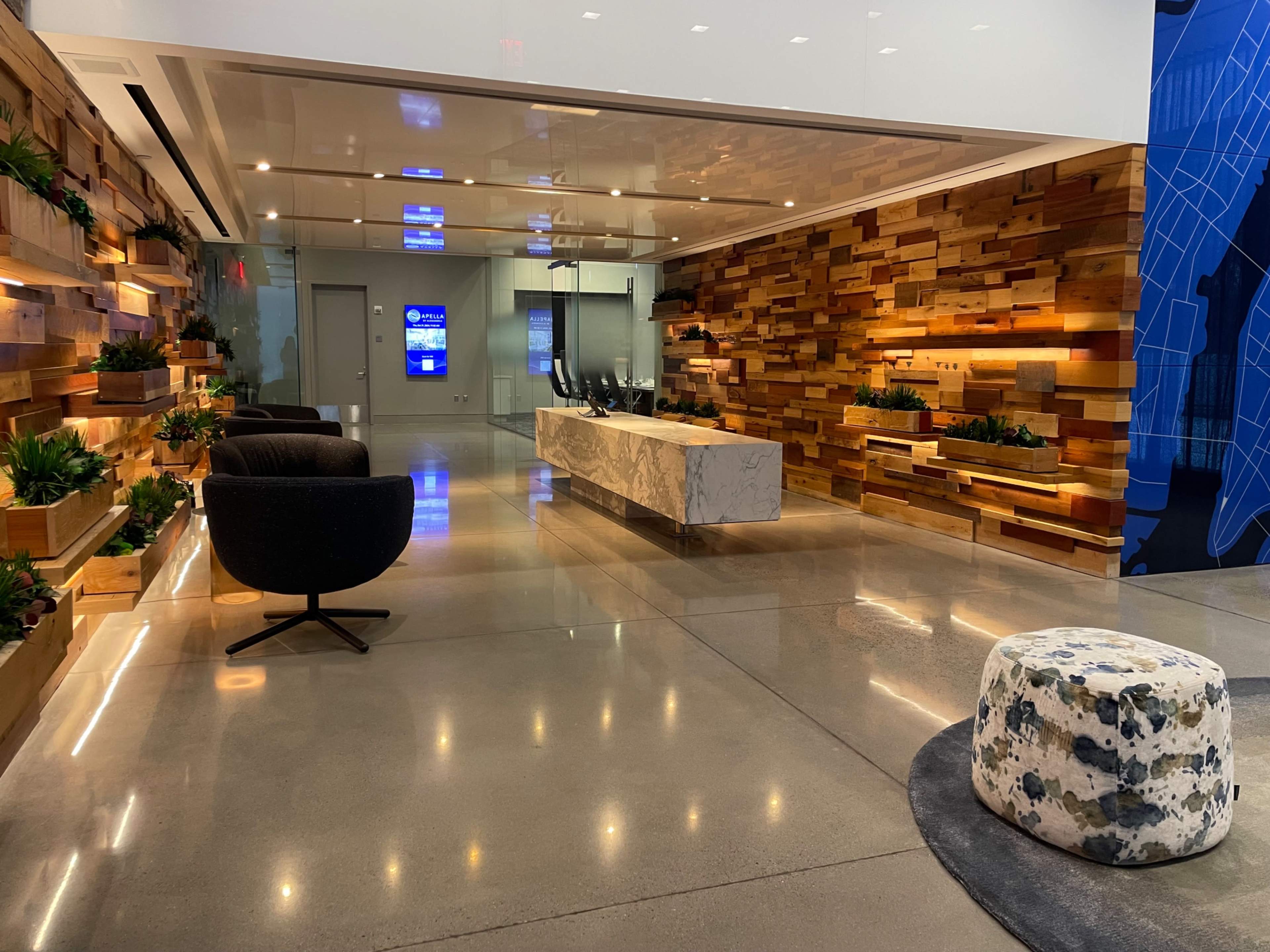 The image shows a modern reception area with wooden accent walls, potted plants, seating arrangements, and a marble reception desk.