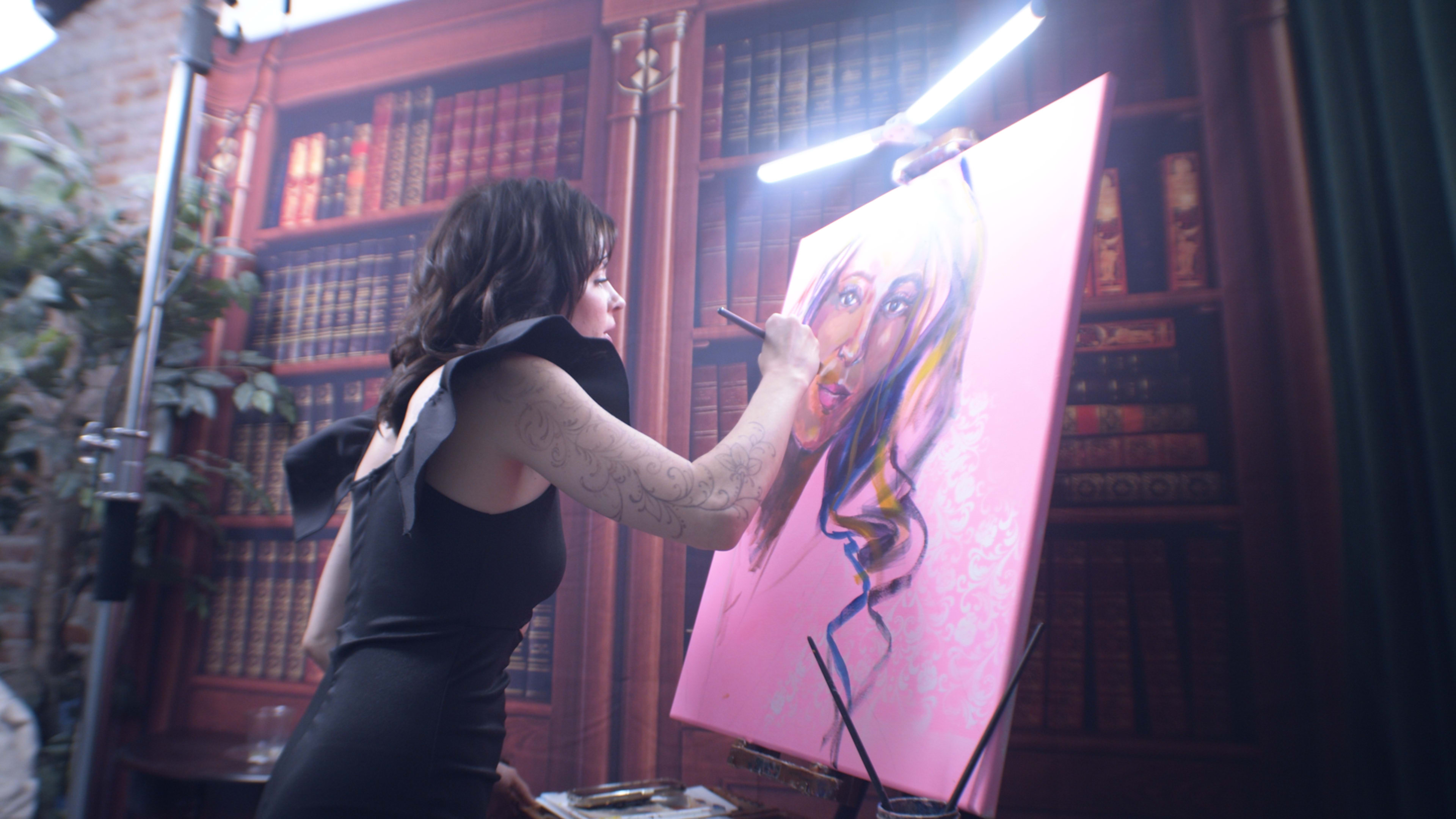 An artist is painting a portrait on a large canvas in front of a backdrop resembling a library.