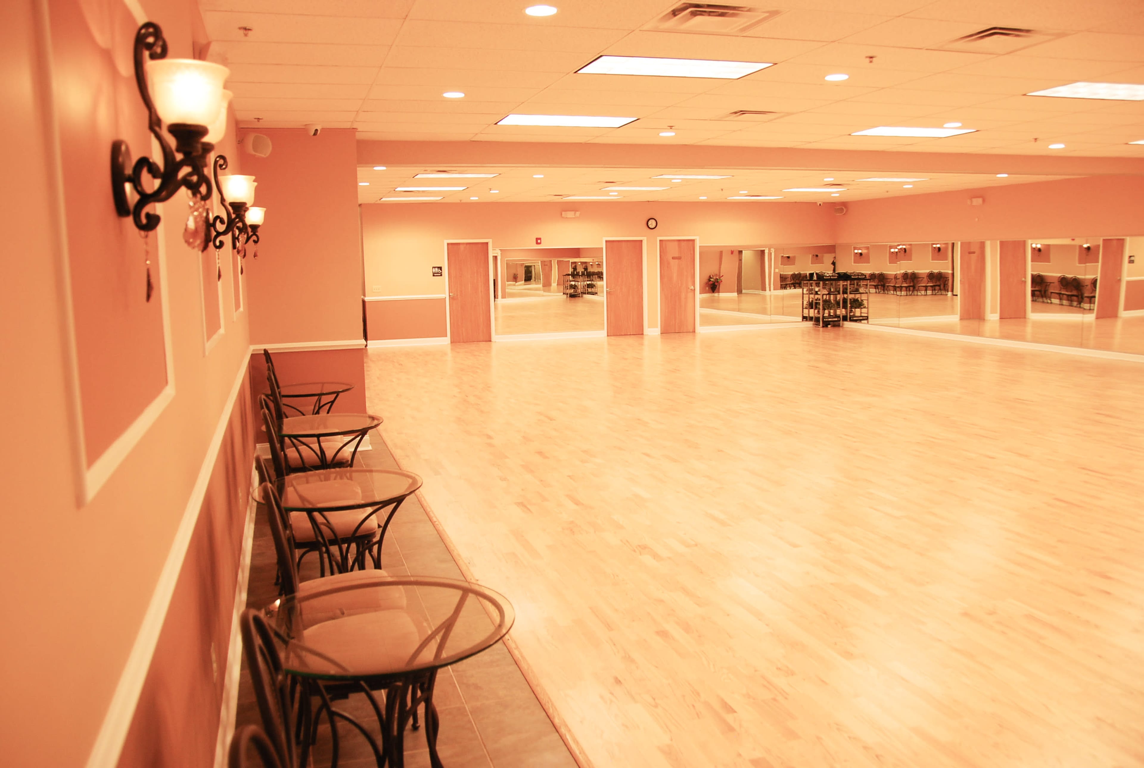 A spacious dance studio with wooden flooring, mirrored walls, and seating along one side.