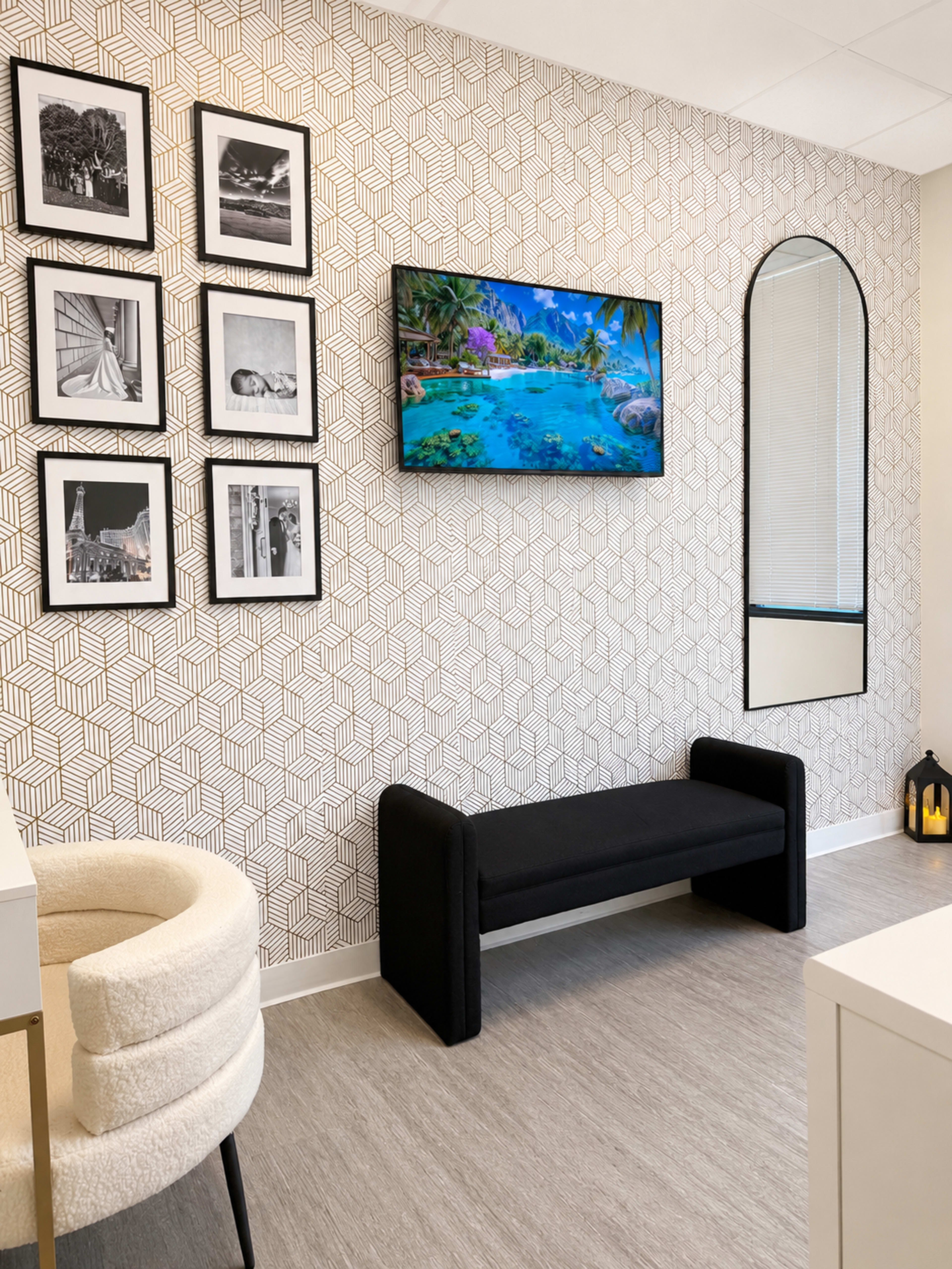The image shows a modern waiting area with a patterned wall, a flat-screen TV displaying a tropical scene, a black bench, and framed black-and-white photos.