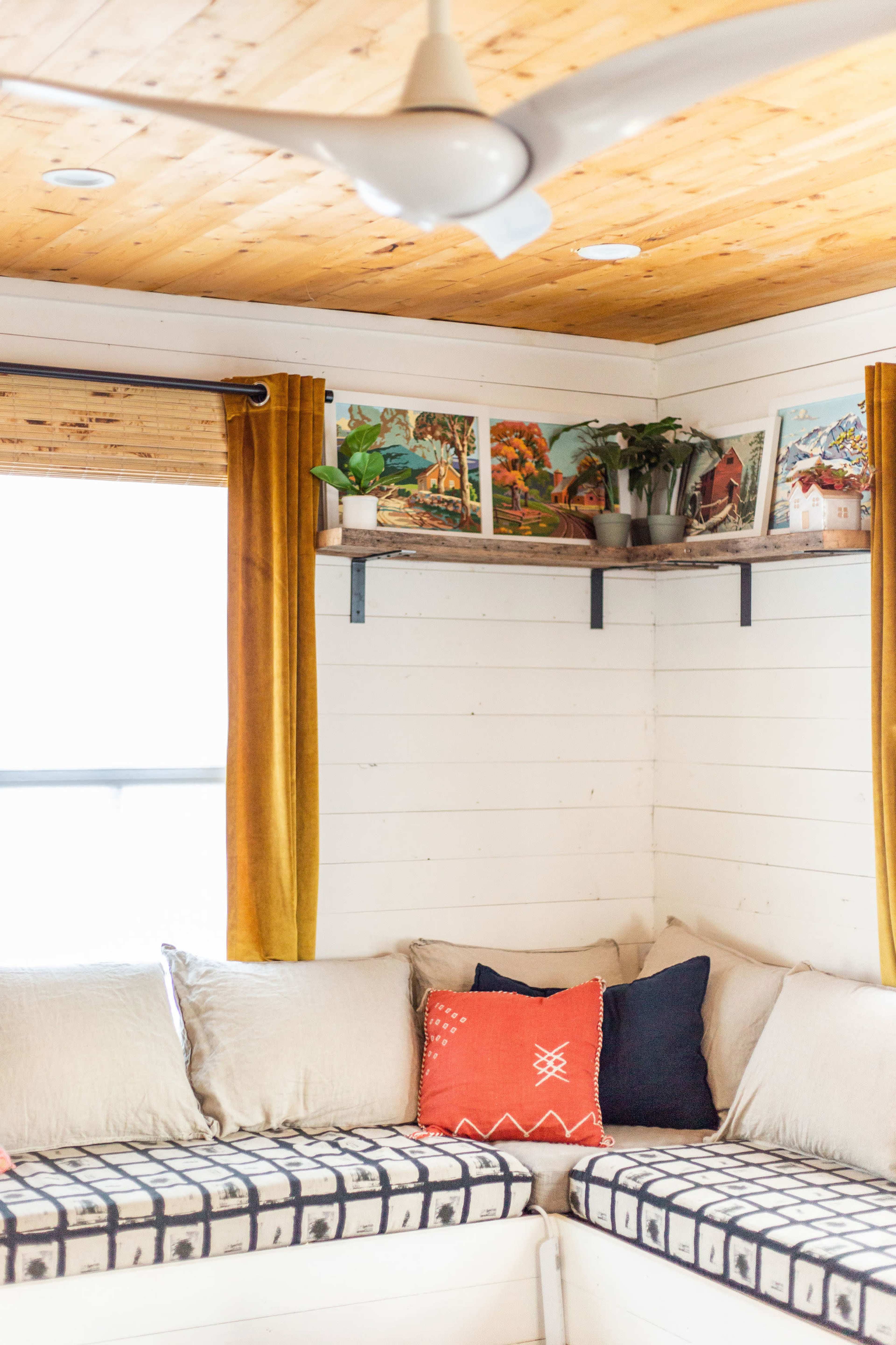 A corner of a room with a cushioned seating area, wooden ceiling, and framed artwork on the wall above a shelf.