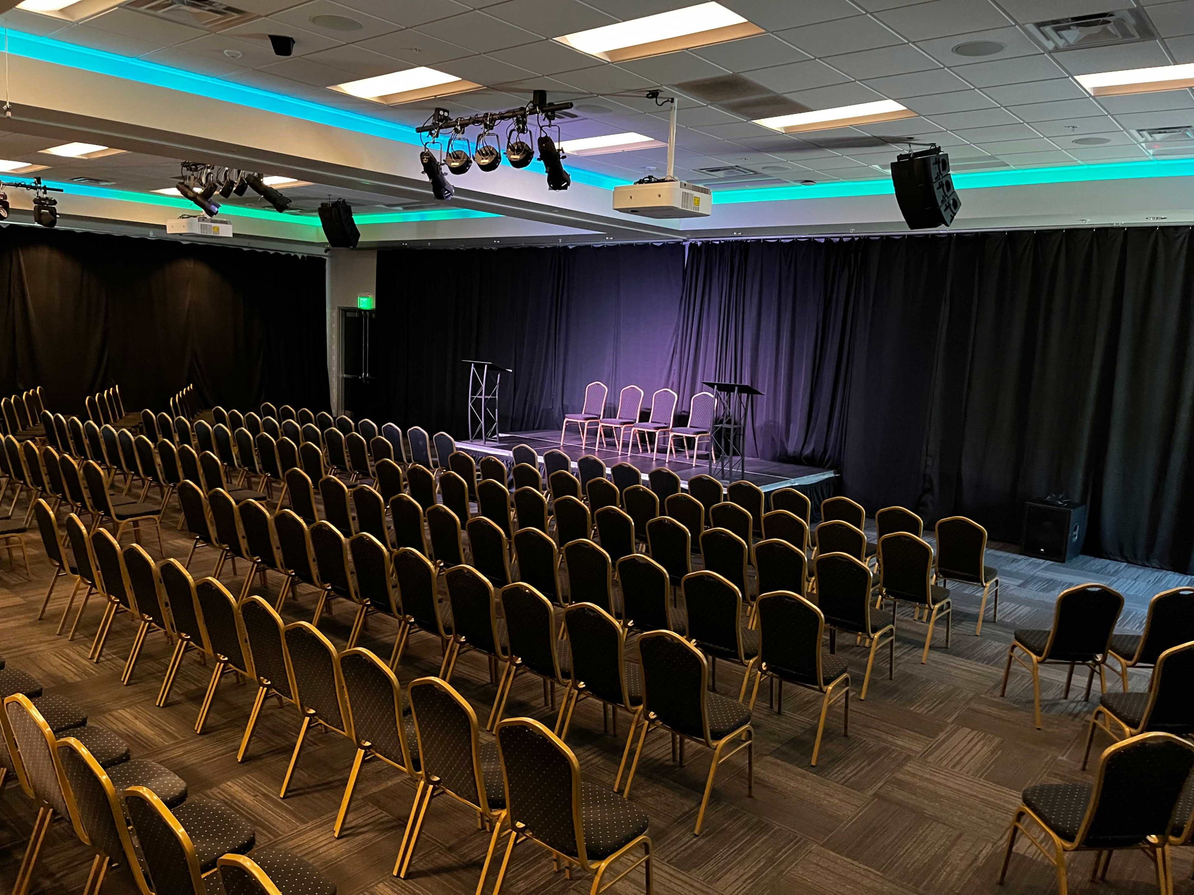A large seminar room set up with rows of empty chairs facing a stage with a podium and microphones.