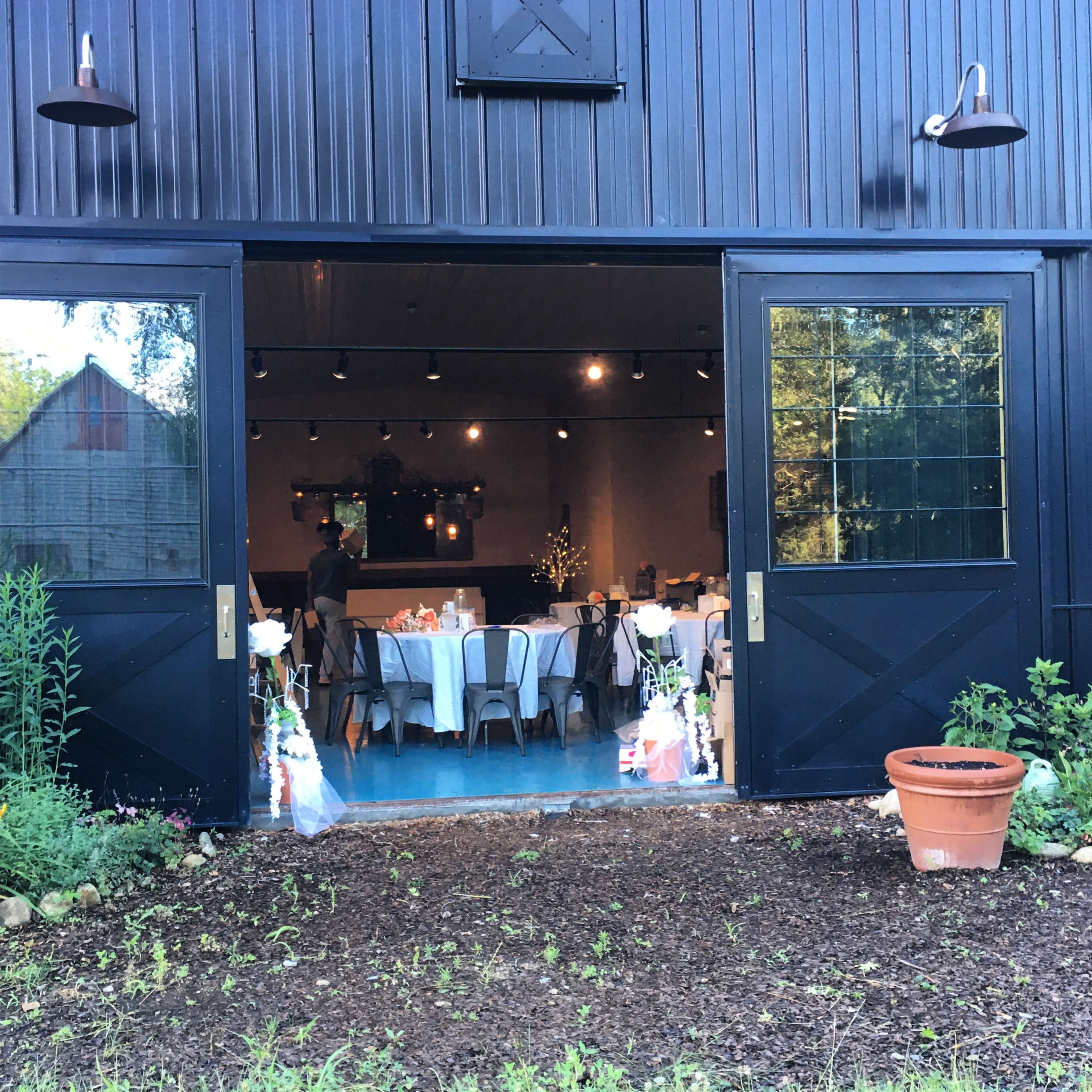 A large barn-style venue is set up for an event, with tables arranged inside and decorative flowers at the entrance.