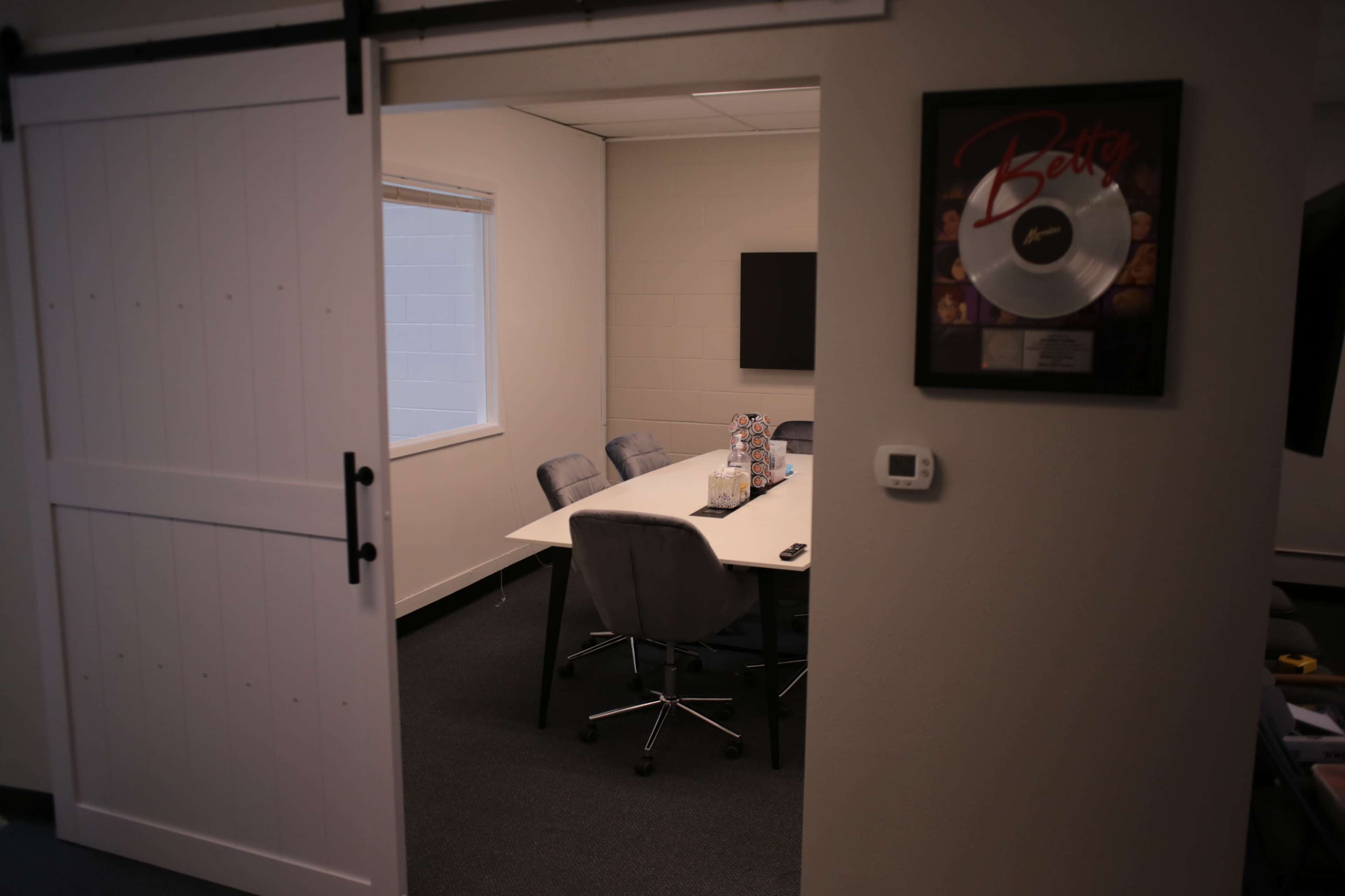 A conference room is visible through an open sliding door, featuring a white table surrounded by gray chairs and a wall-mounted screen.
