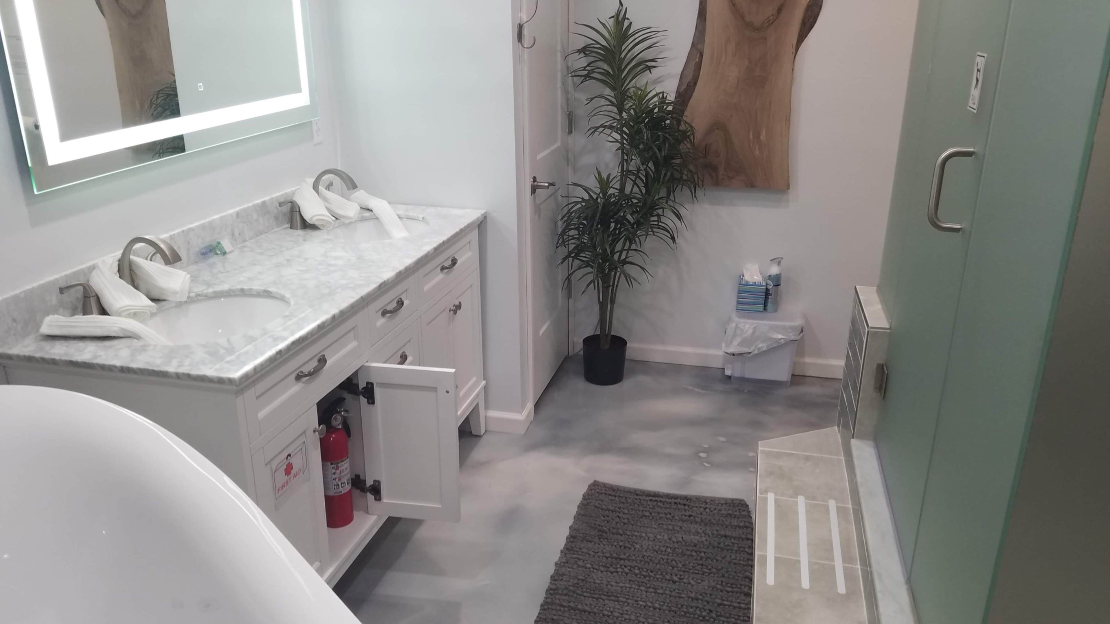 A modern bathroom featuring a marble countertop, a plant, and a glass shower enclosure.