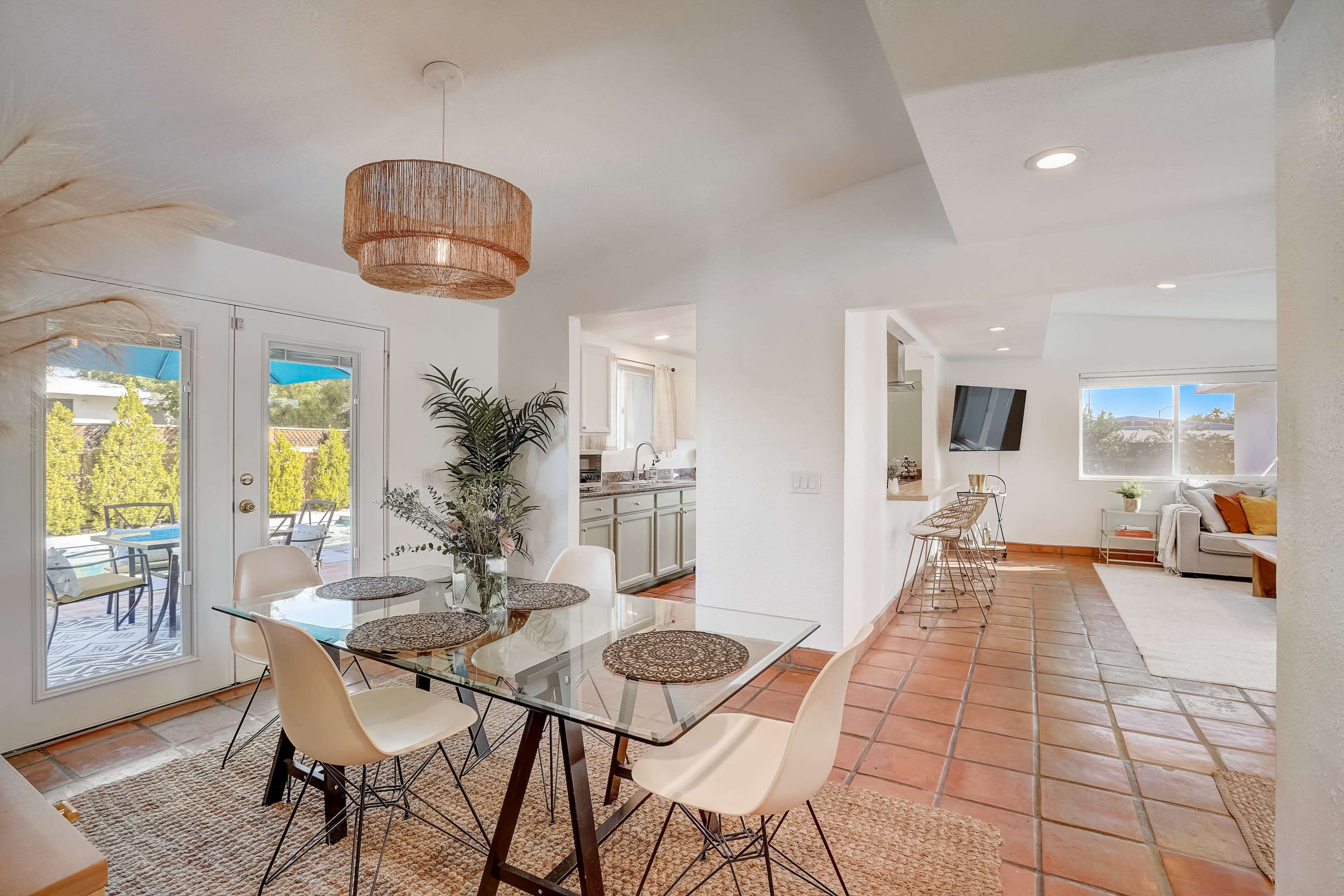 A bright dining area features a glass table with six chairs, surrounded by a modern kitchen and a living room visible in the background.