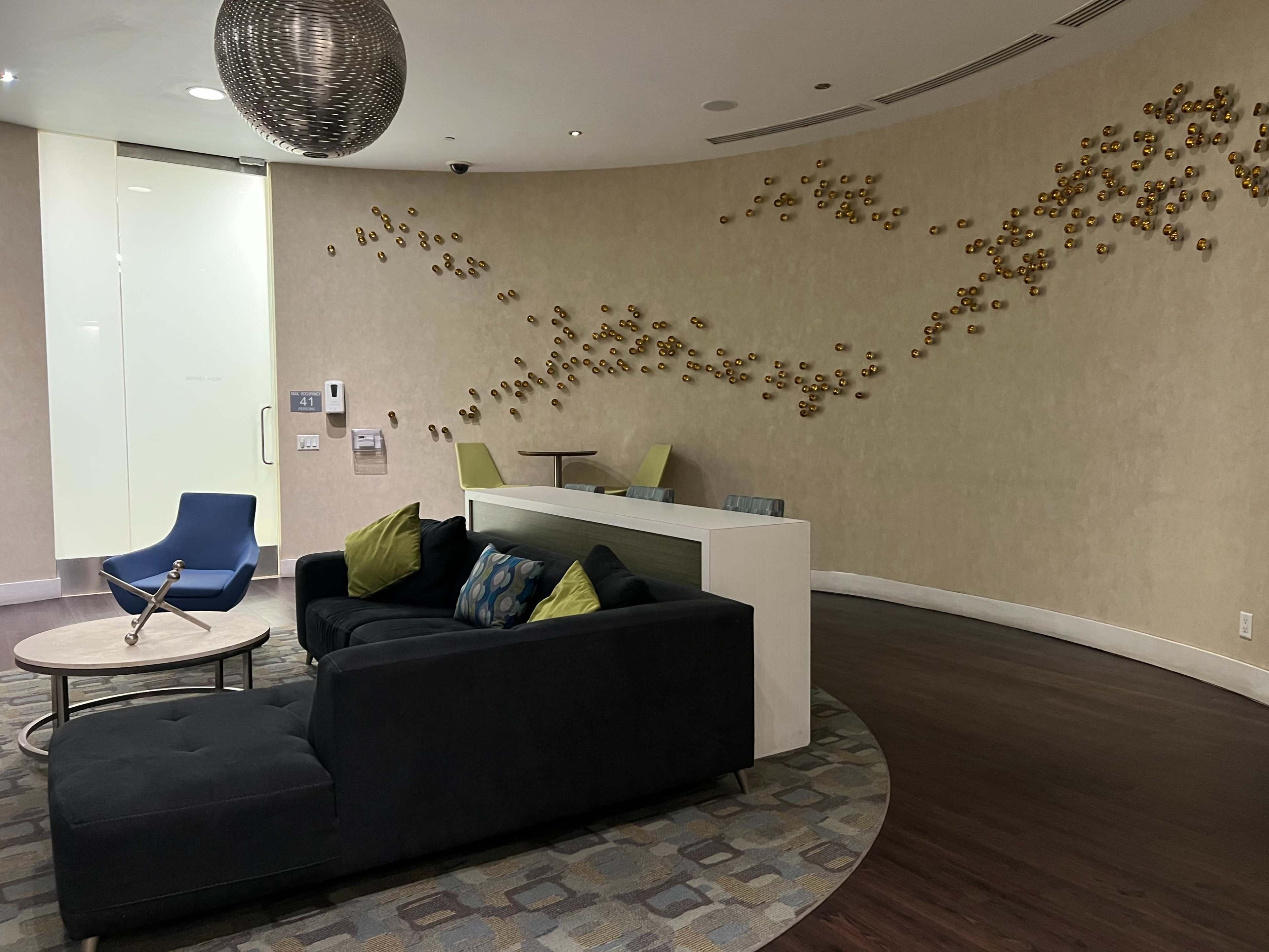 A modern lounge area features a dark sofa, a circular table, and decorative wall art made of gold spheres.