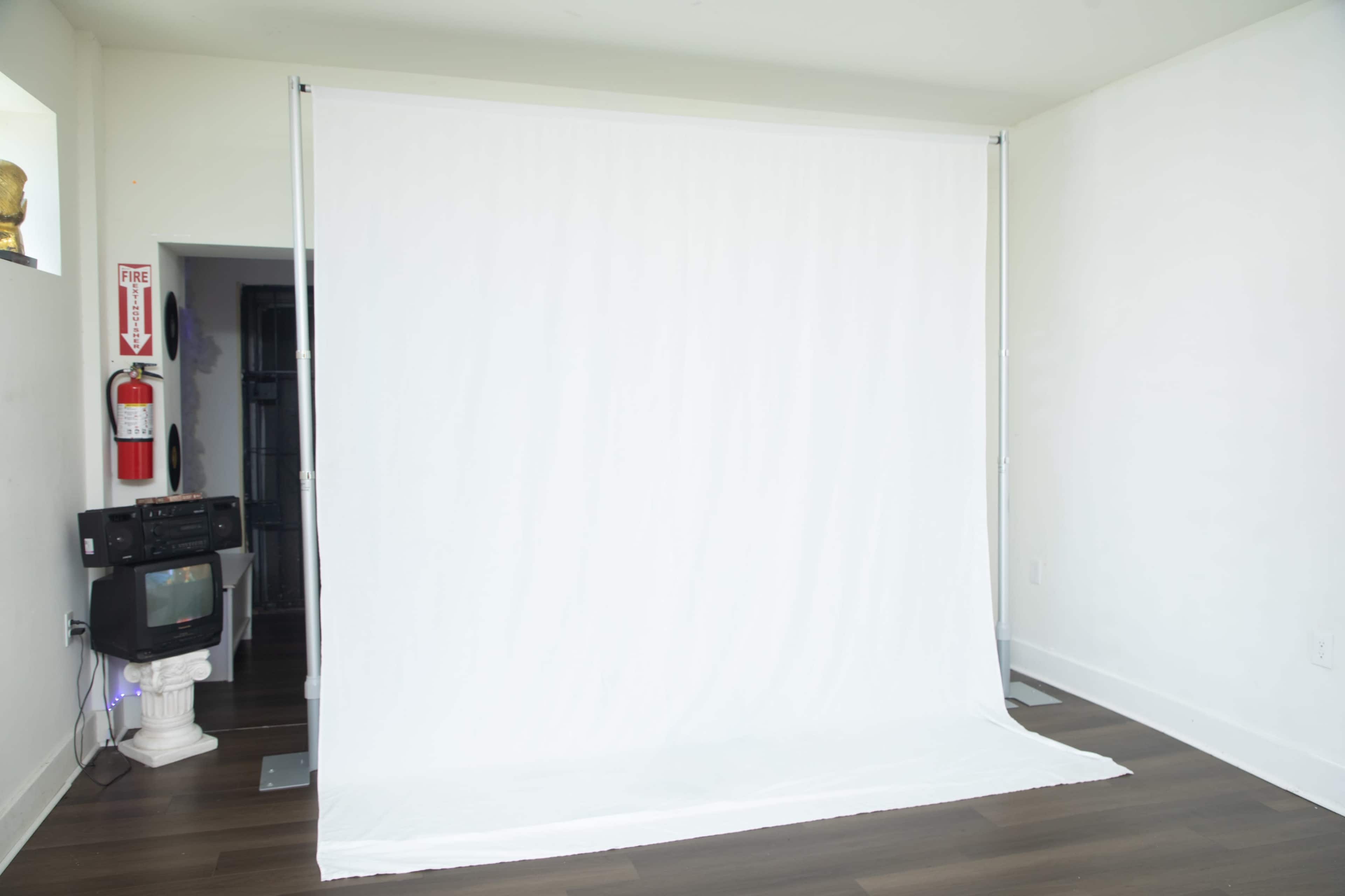 The image shows a plain white backdrop set up in a well-lit room with wooden flooring.