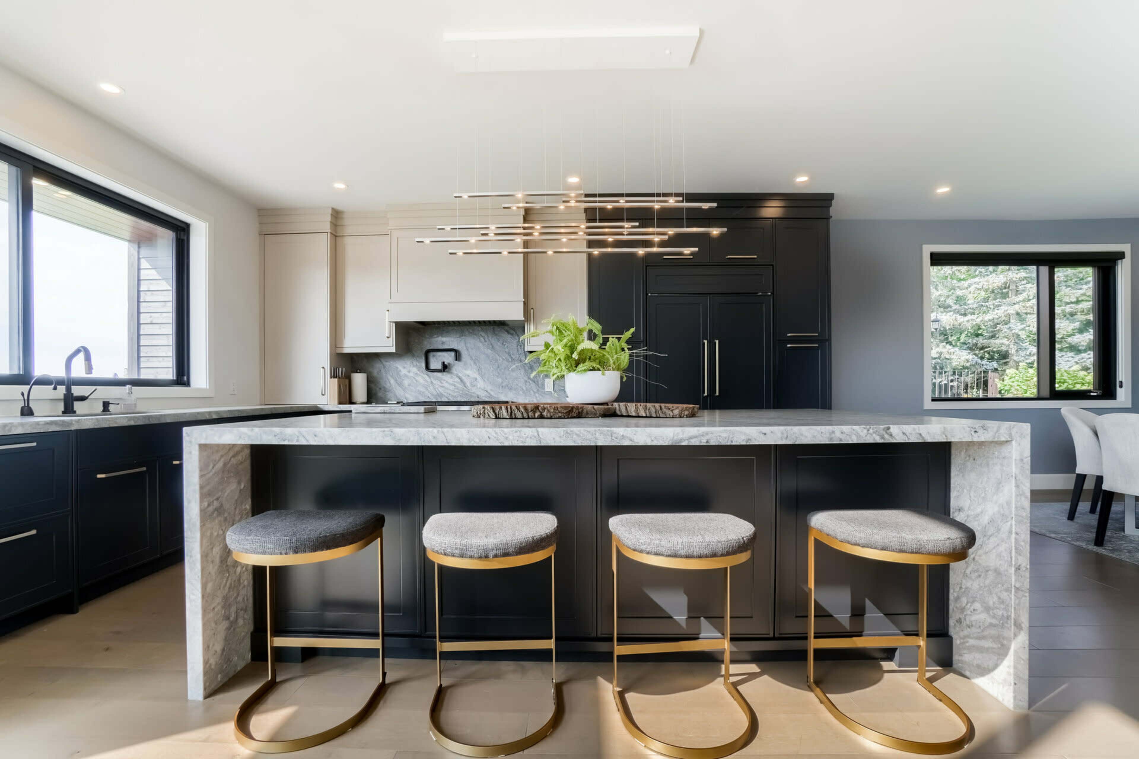A modern kitchen featuring a large marble island with four gold-accented bar stools and sleek black cabinets.