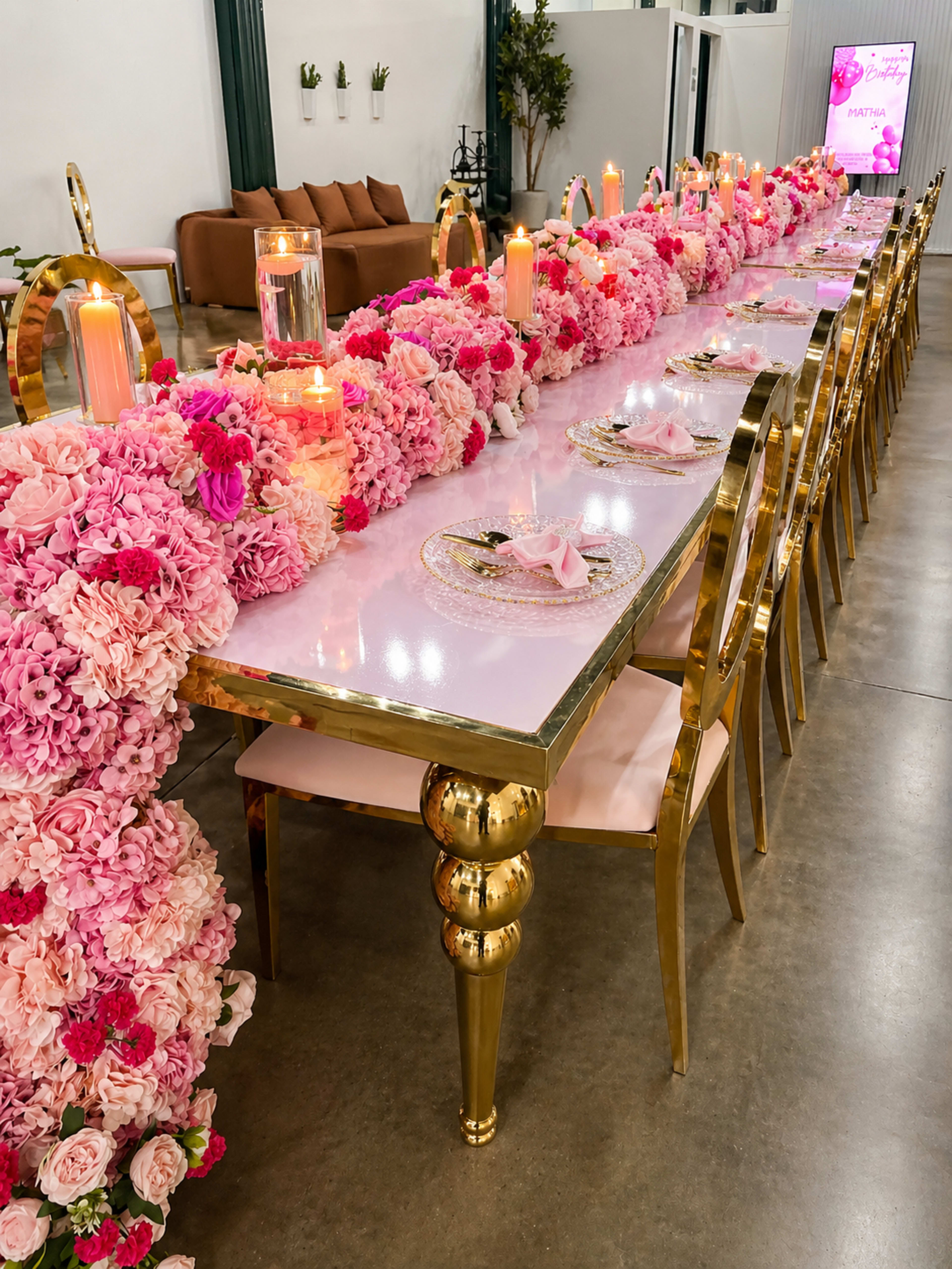 A long table is decorated with pink flowers and candles, set in a modern venue with a stylish seating area in the background.