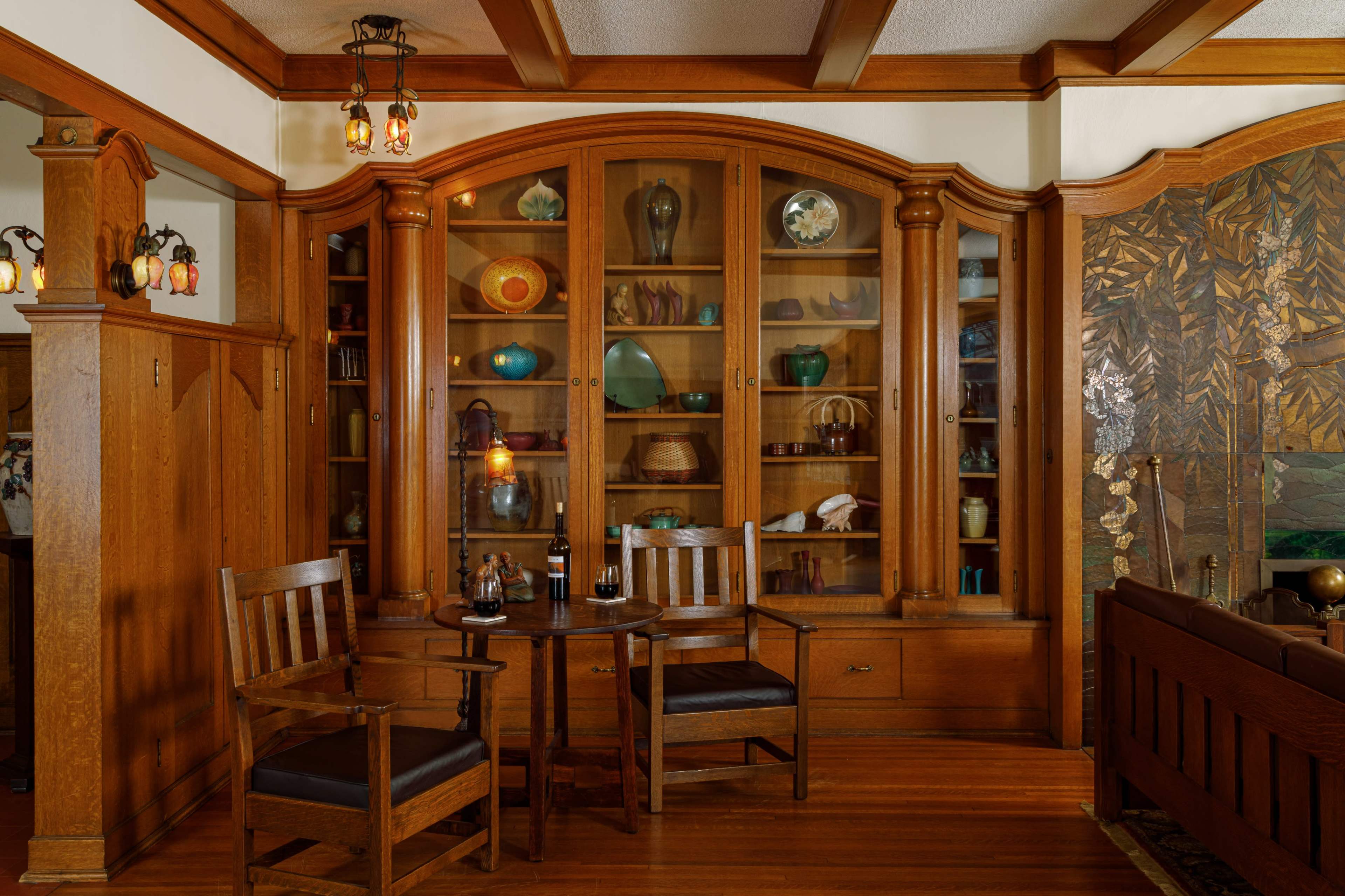 A cozy seating area features two wooden chairs and a small table in front of a curved display cabinet filled with decorative items.