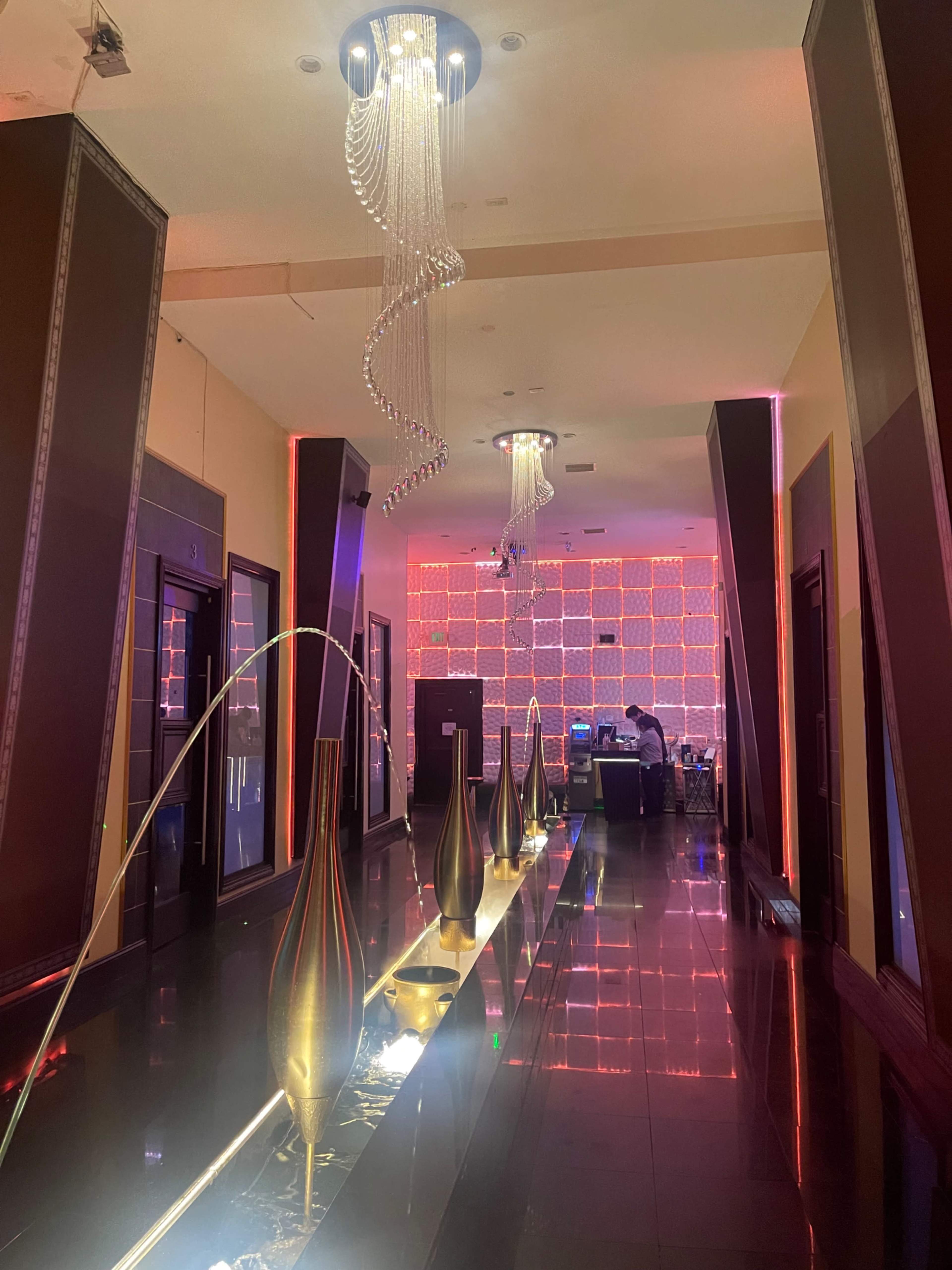 The image shows a modern hallway with decorative lighting, elegant vases, and a vibrant backdrop of red illuminated panels.