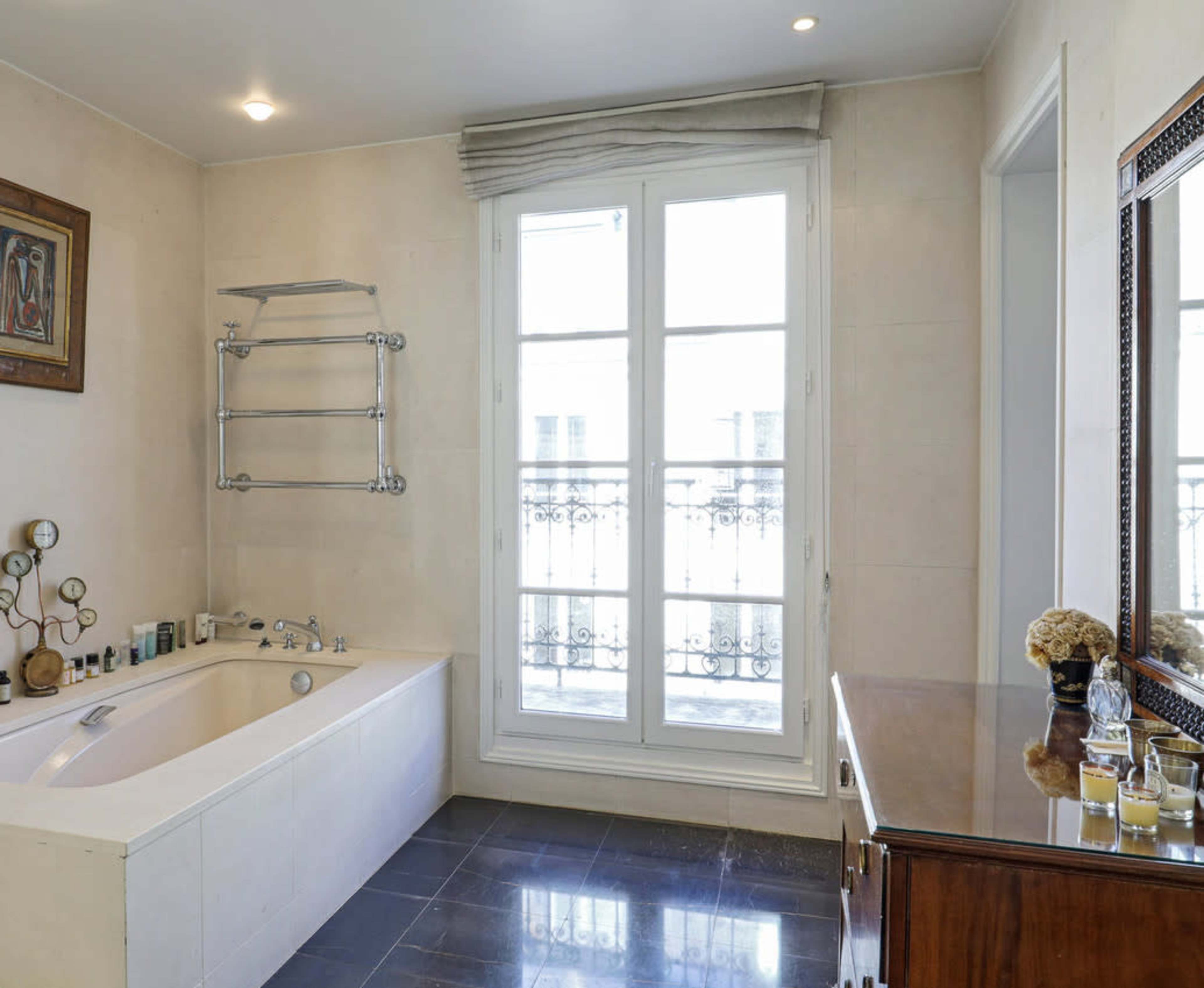The bathroom features a freestanding bathtub, a wall-mounted towel rack, and a wooden vanity, with large windows providing natural light.