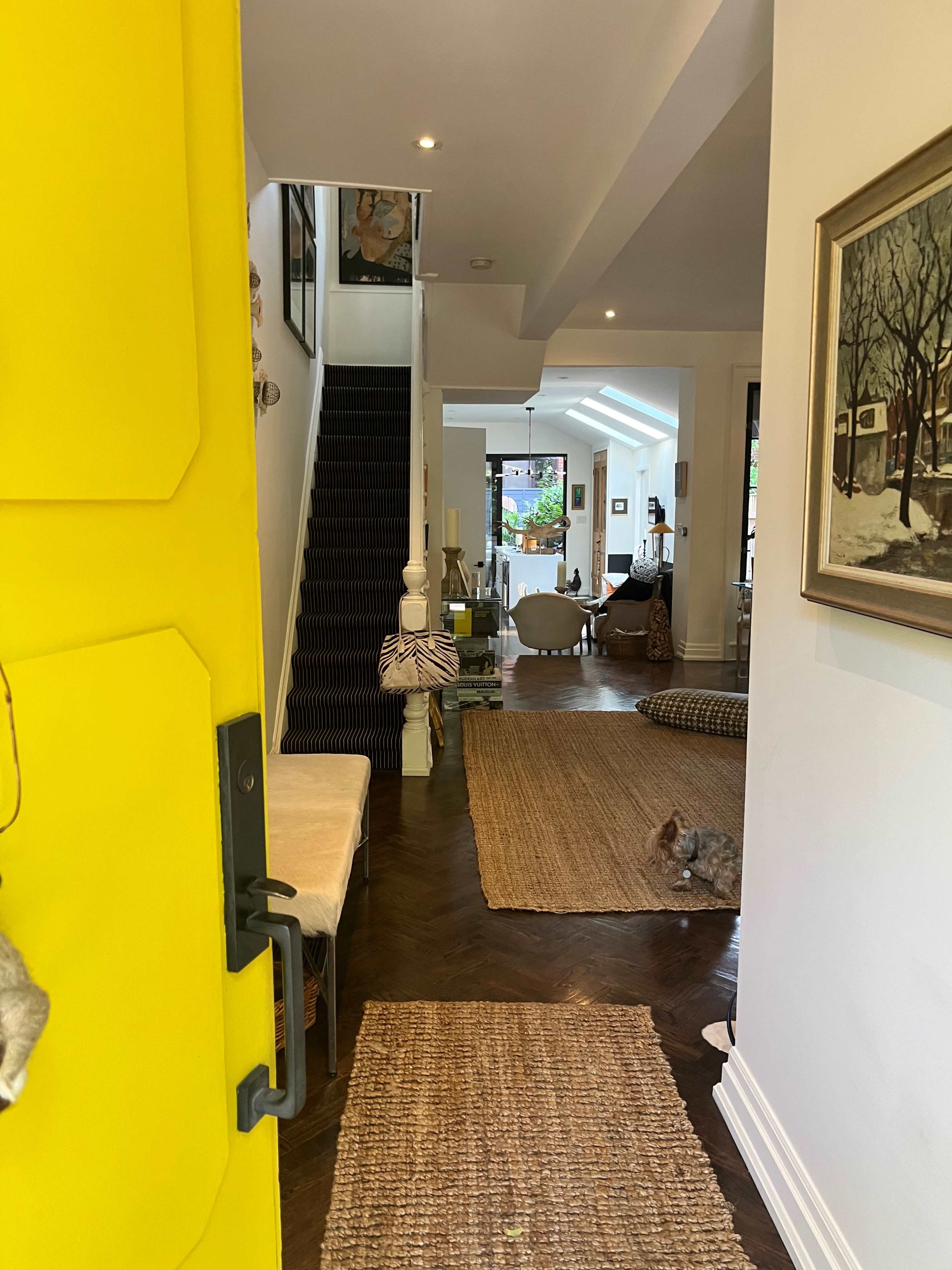 A bright yellow door provides a view into a cozy interior hallway that leads to a staircase and an adjacent living area.