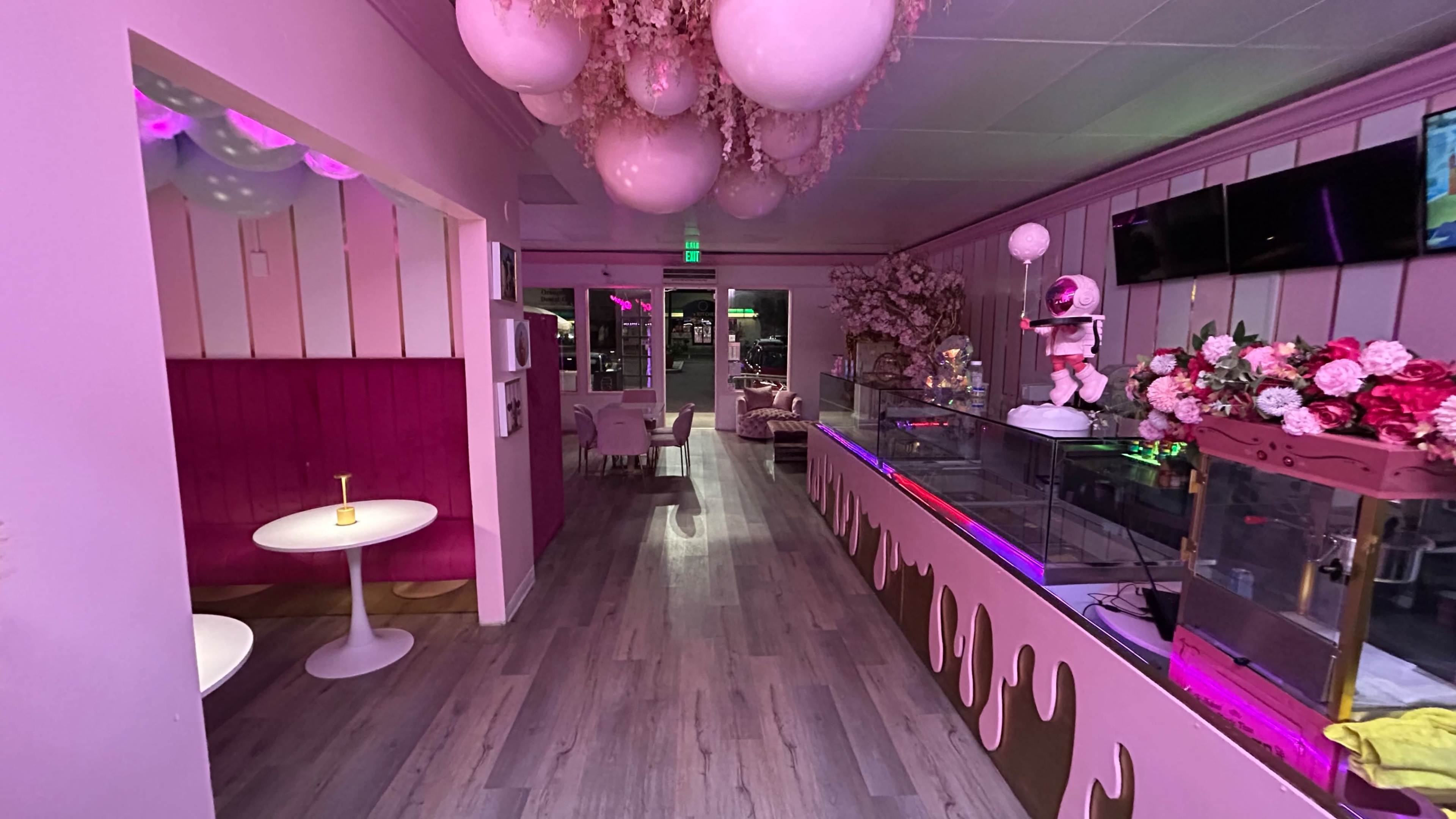 The image shows a pink-themed café interior with decorative balloons, a display counter, and seating areas.