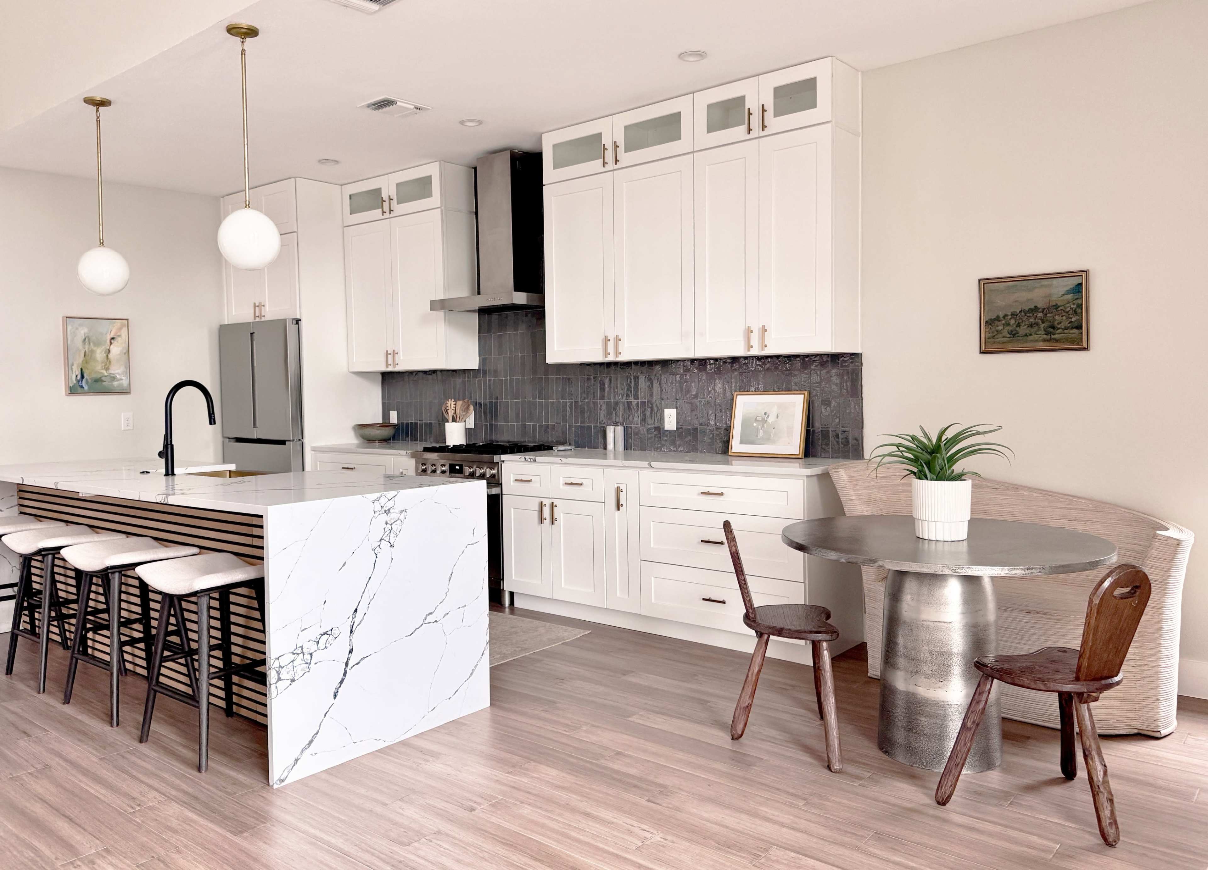 A modern kitchen features white cabinetry, a marble island with bar seating, and a circular metal dining table surrounded by wooden chairs.