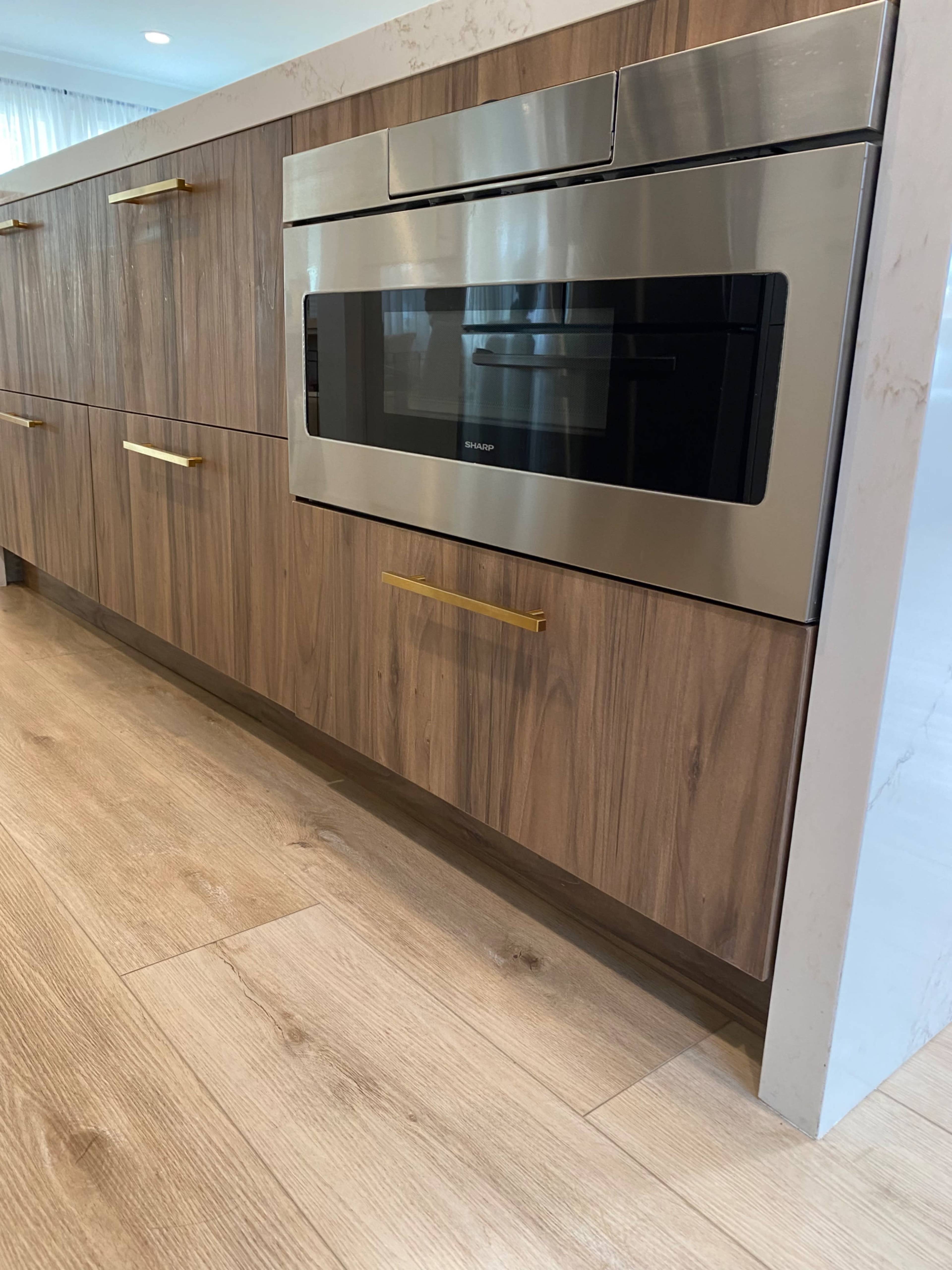A kitchen interior featuring wooden cabinetry with a built-in microwave and brass handles on the drawers.