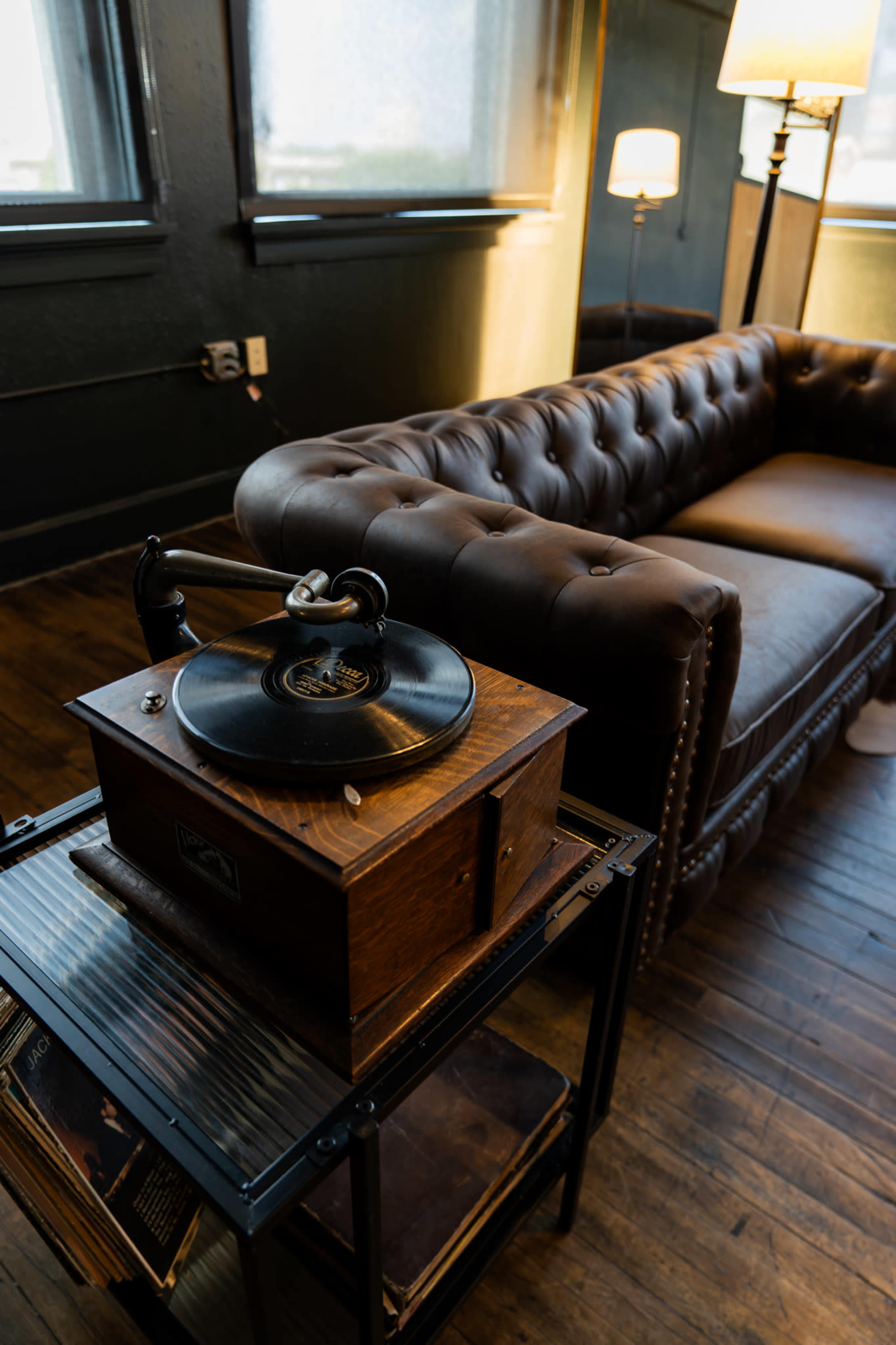 A vintage record player sits on a wooden stand next to a tufted leather sofa in a well-lit room.