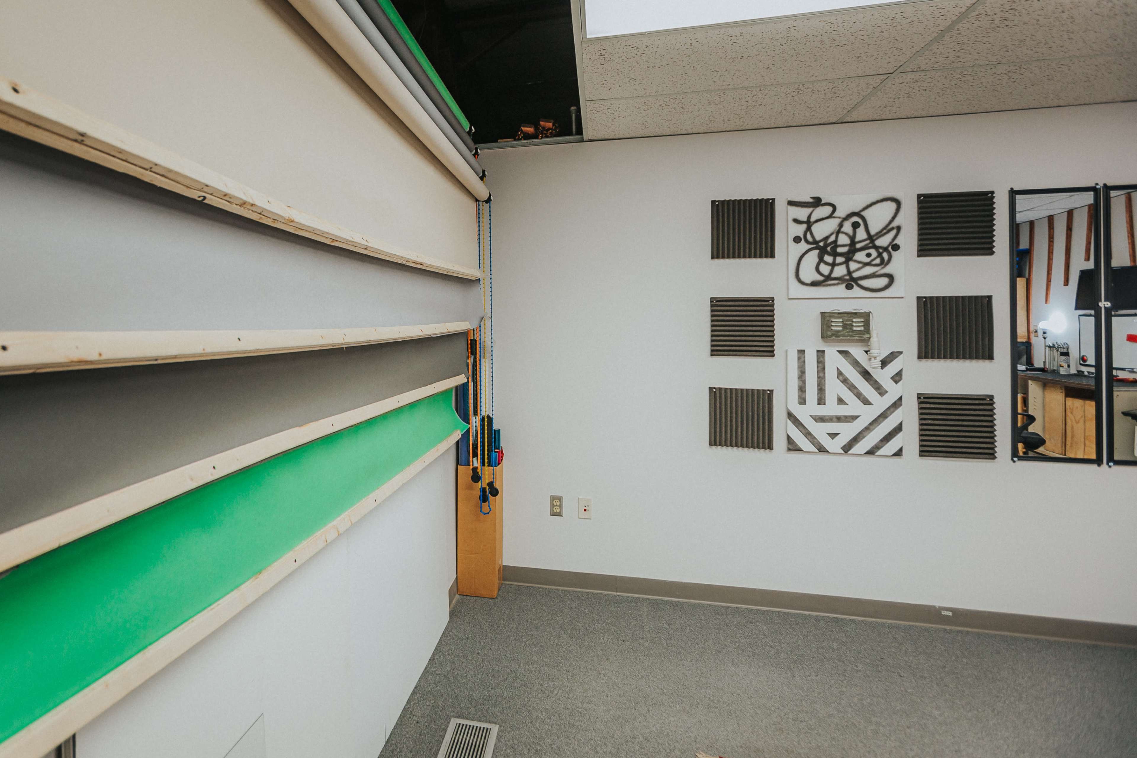 A room with a green screen wall, various mounted panels, and a mirror arranged on one side.