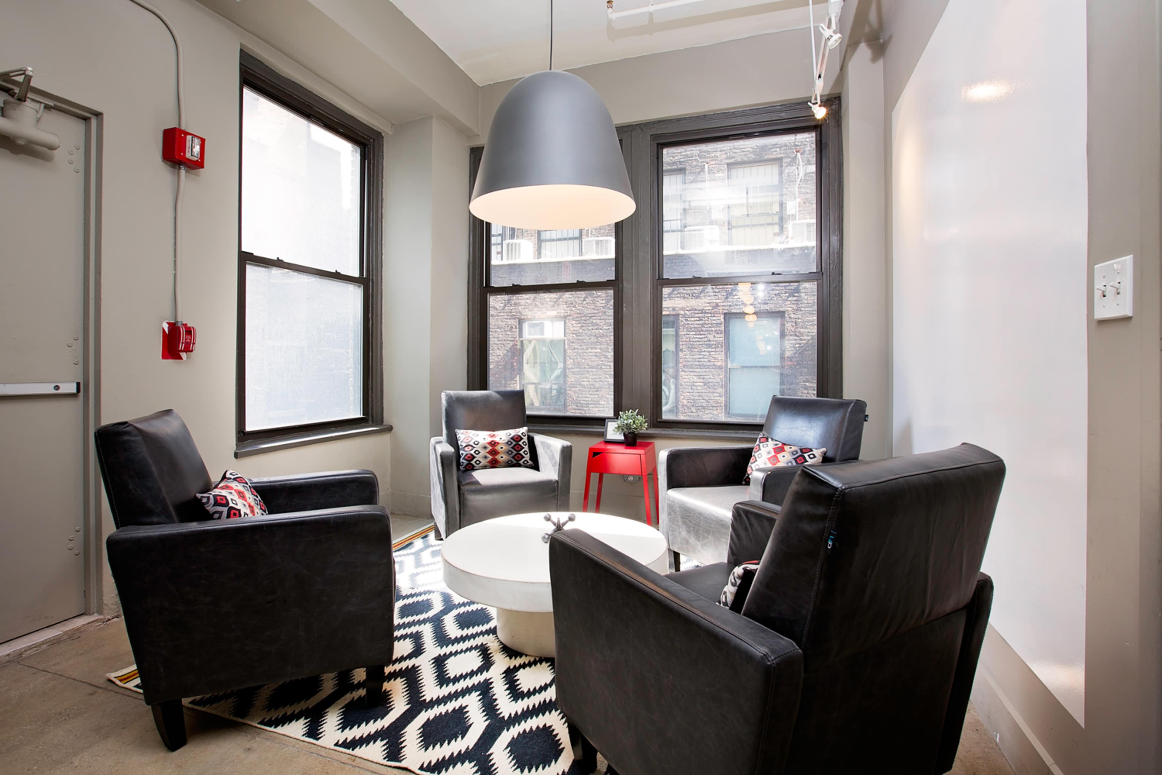 The image shows a modern seating area with four black chairs arranged around a circular coffee table, positioned on a patterned rug under a large pendant light.