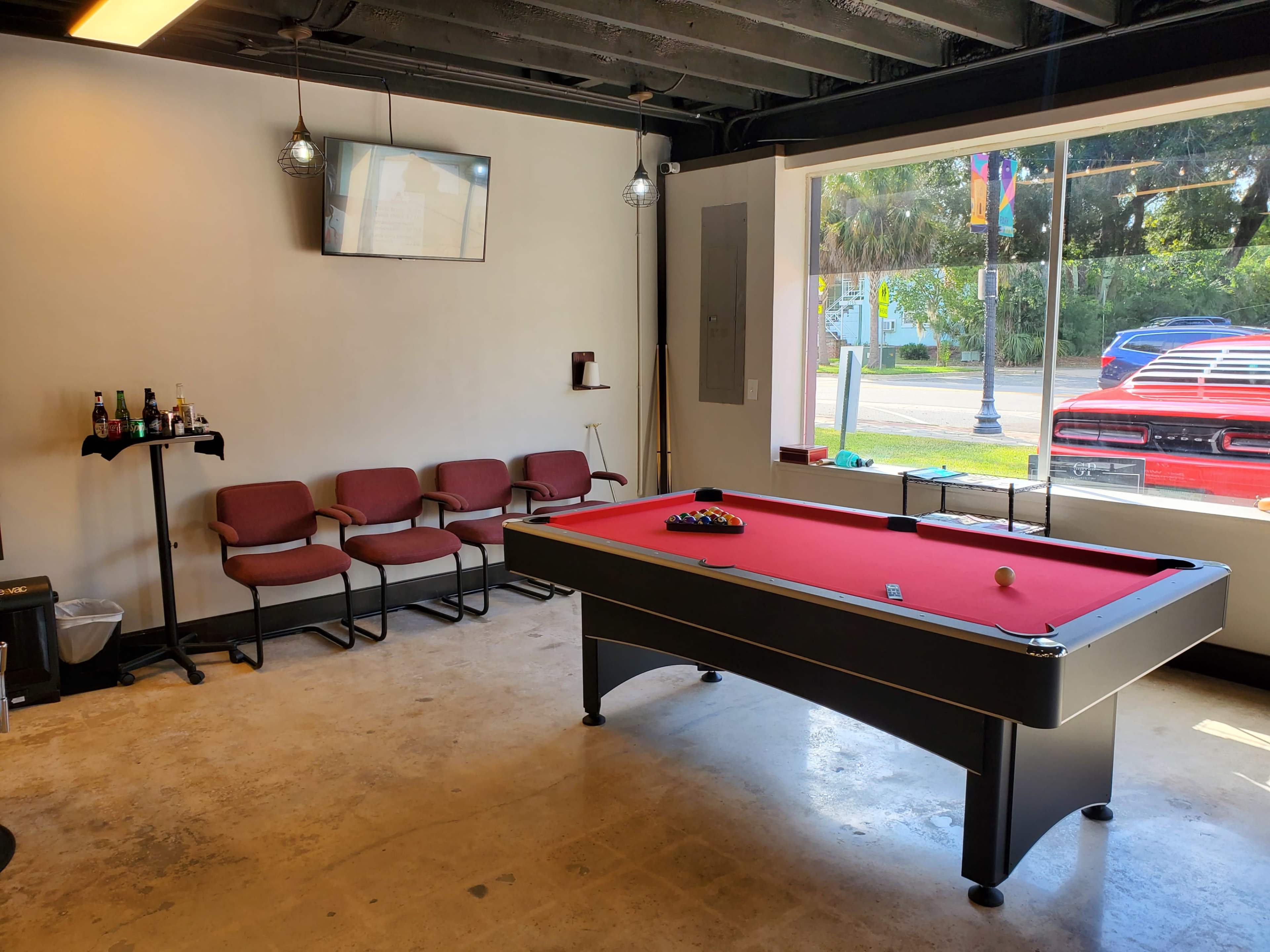 The image shows a room featuring a red pool table centrally located, with several chairs against the wall and a television mounted above.