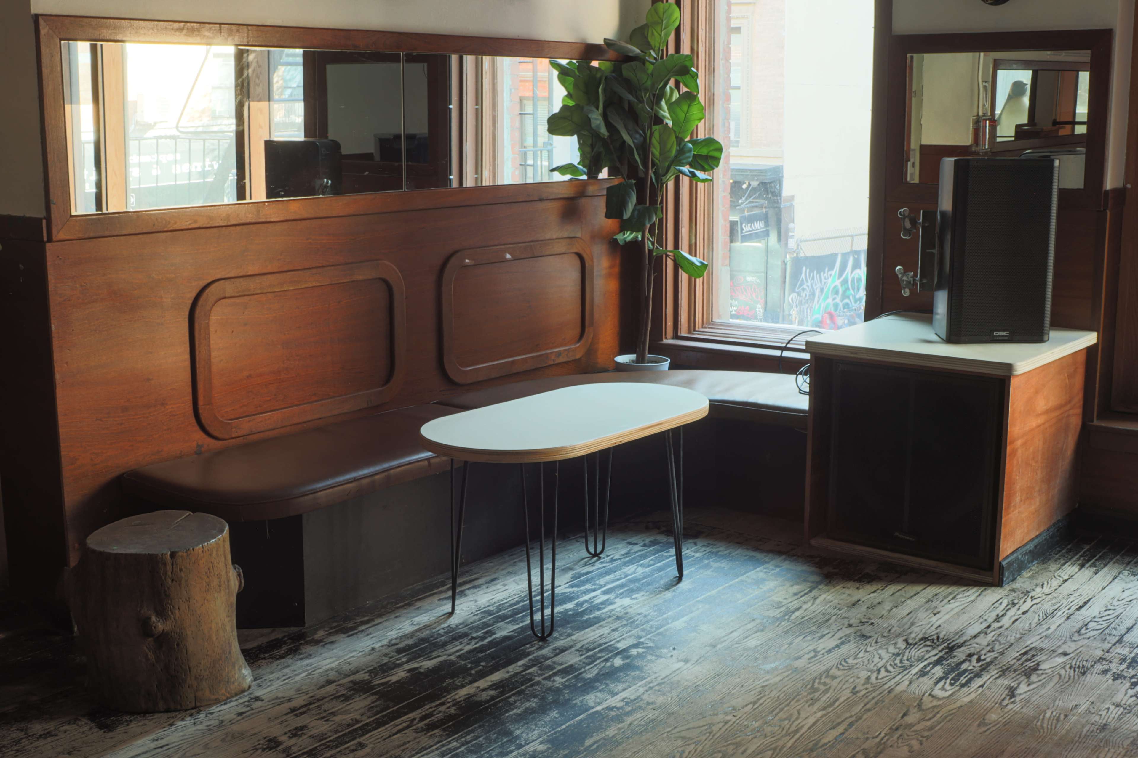 A cozy seating area in a room with wooden benches, a round table on slender legs, and a large speaker next to a window.