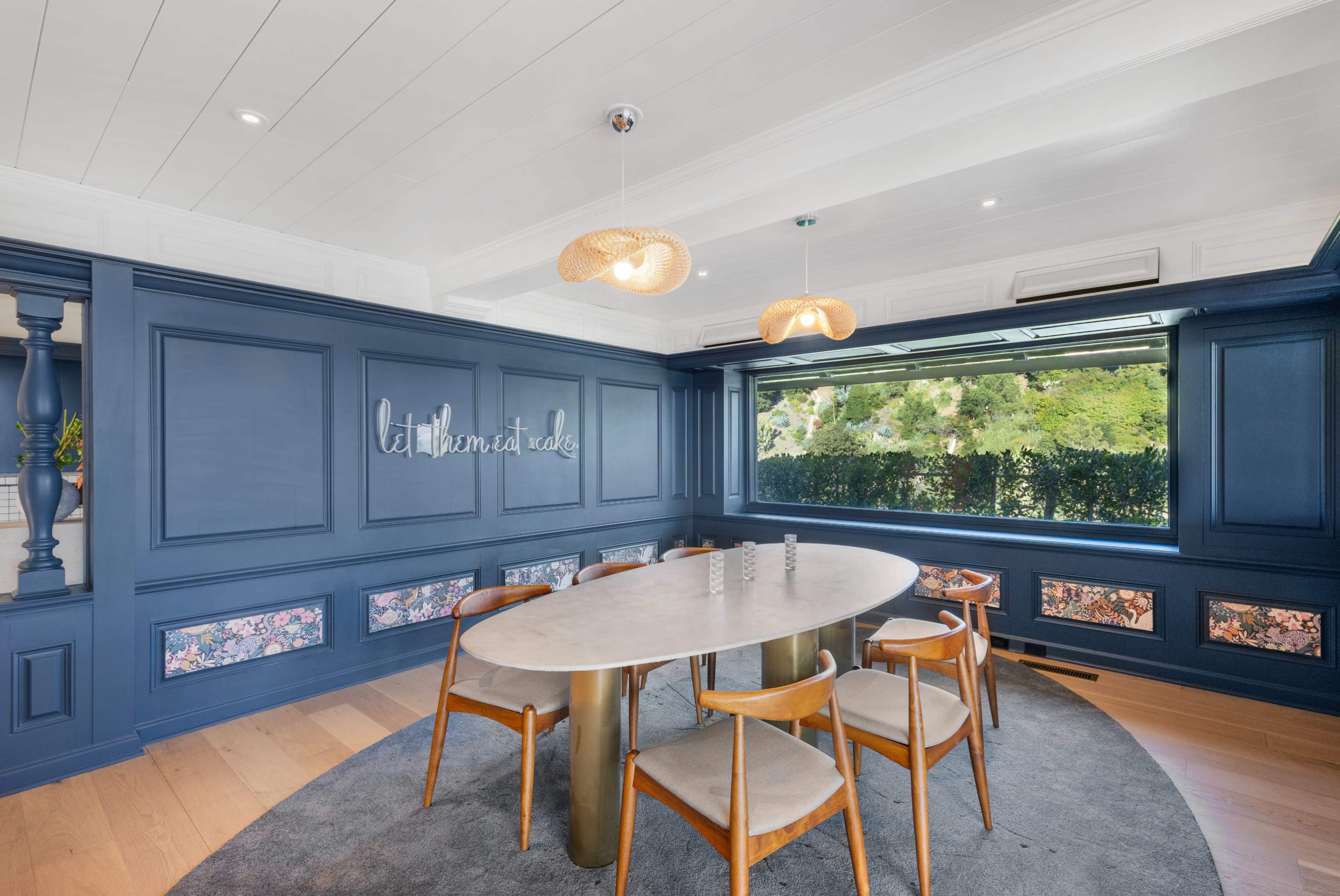 A round marble table with wooden chairs is set in a room featuring navy blue walls and large windows that overlook a green landscape.